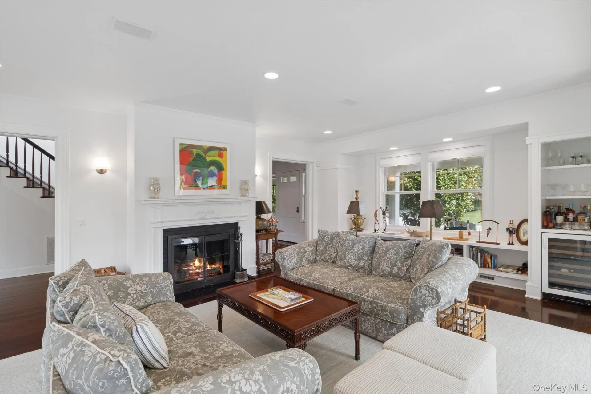 Living area with dark wood-style floors, beverage cooler, ornamental molding, recessed lighting, and a glass covered fireplace Living area with dark wood-style floors, beverage cooler, ornamental molding, recessed lighting, and a glass covered fireplace