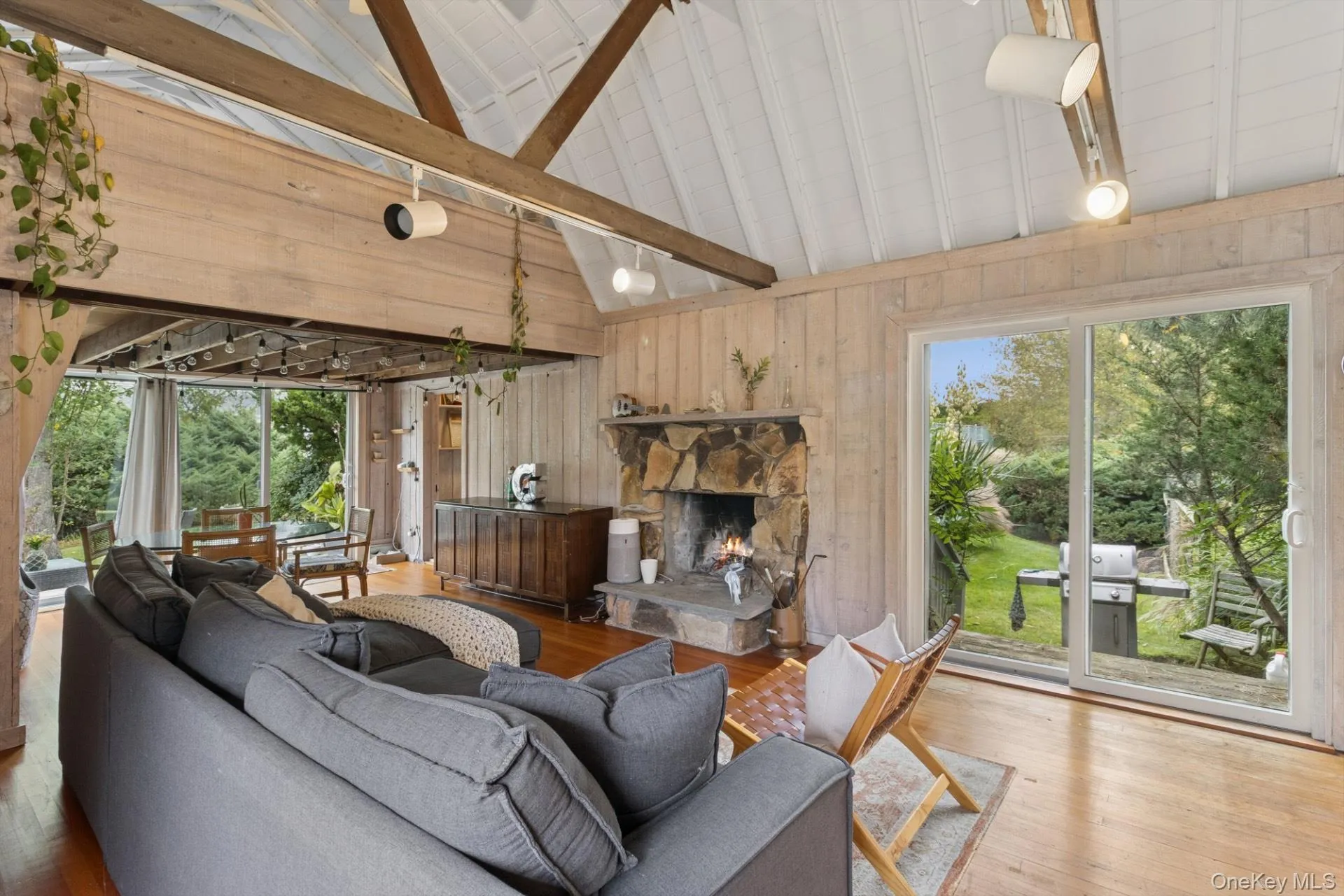 Living area with wooden walls, beamed ceiling, healthy amount of natural light, a stone fireplace, and high vaulted ceiling Living area with wooden walls, beamed ceiling, healthy amount of natural light, a stone fireplace, and high vaulted ceiling