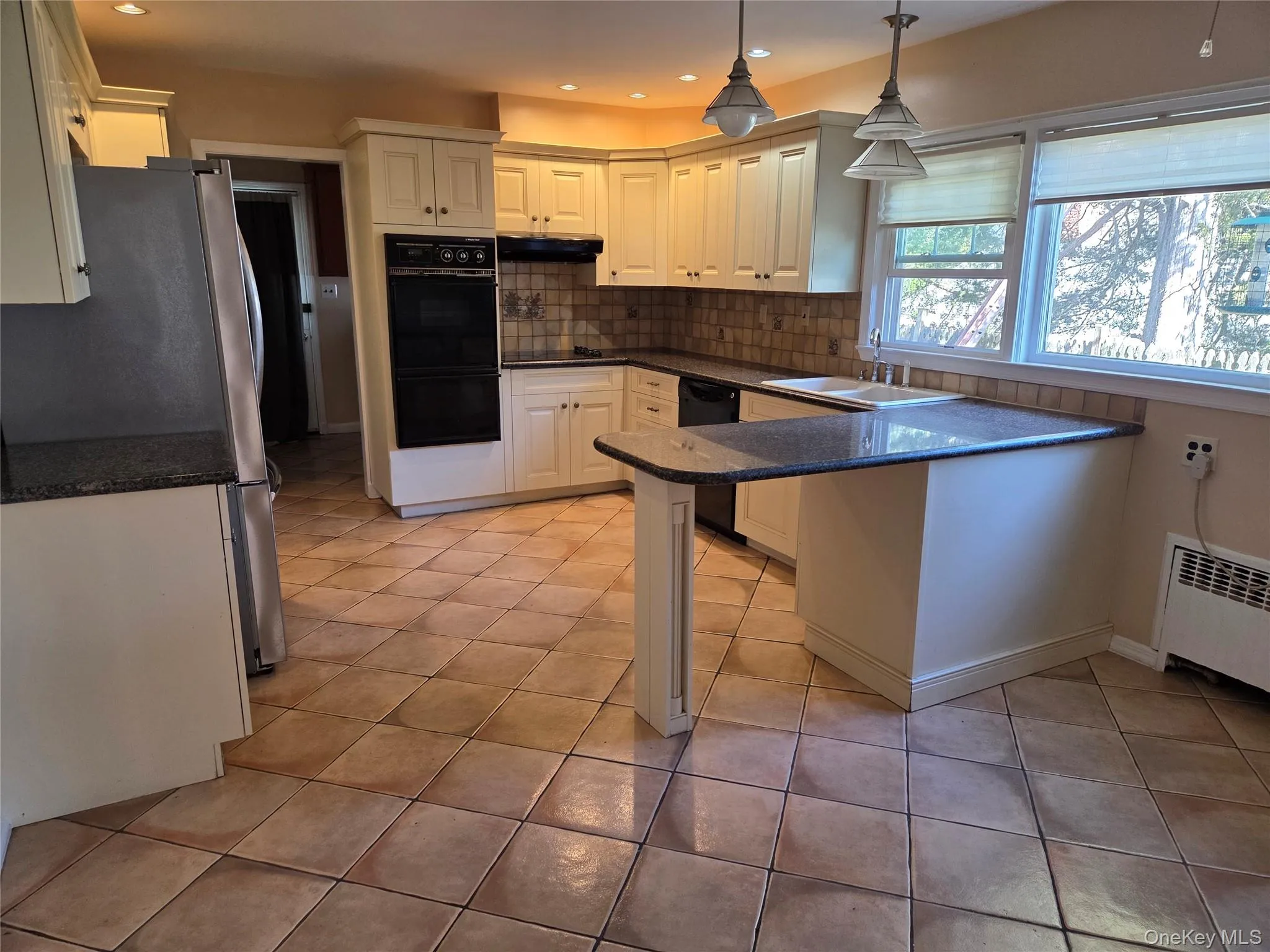 Kitchen with black appliances, hanging light fixtures, dark stone countertops, tasteful backsplash, and a peninsula Kitchen with black appliances, hanging light fixtures, dark stone countertops, tasteful backsplash, and a peninsula