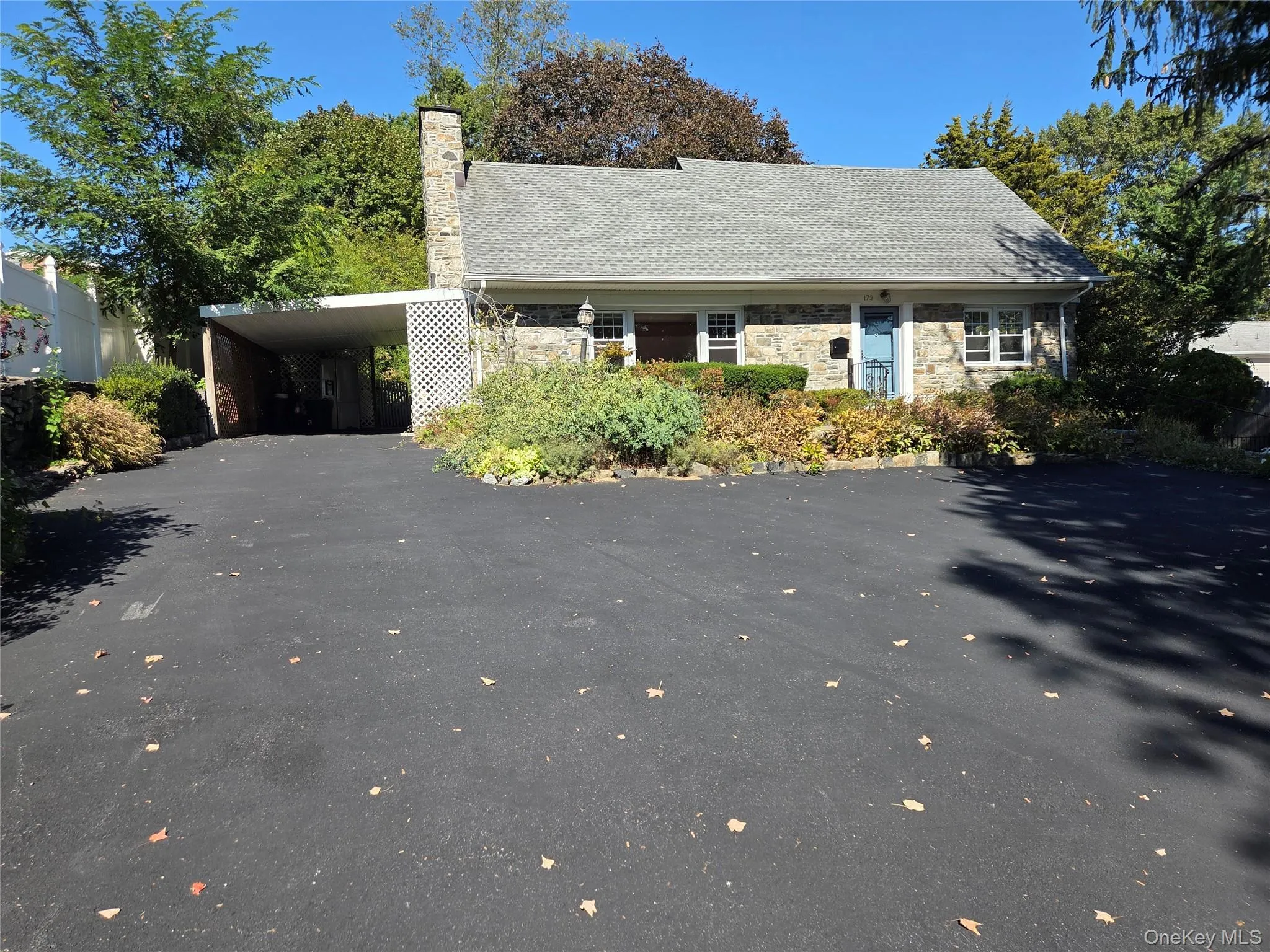 View of front of home with driveway, stone siding, a chimney, an attached carport, and a shingled roof View of front of home with driveway, stone siding, a chimney, an attached carport, and a shingled roof