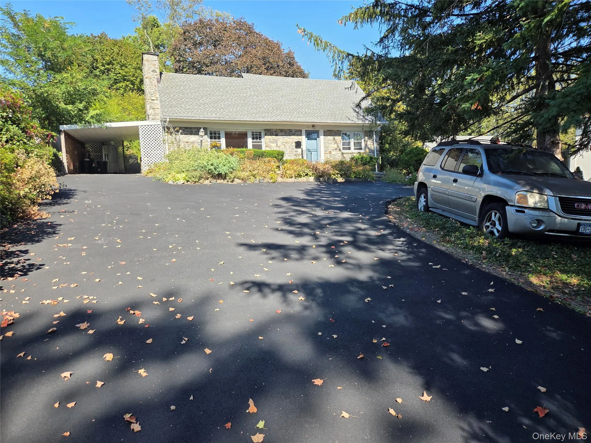 View of front of home featuring driveway, a chimney, stone siding, and an attached carport View of front of home featuring driveway, a chimney, stone siding, and an attached carport