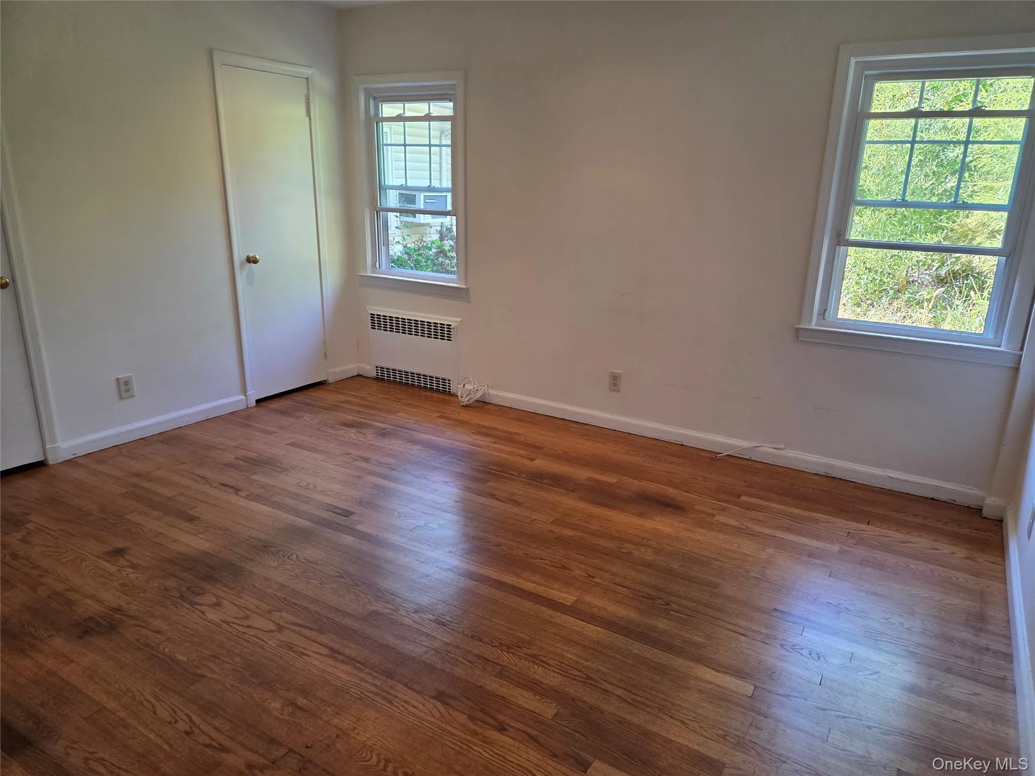 Unfurnished bedroom featuring radiator and dark wood-style floors Unfurnished bedroom featuring radiator and dark wood-style floors