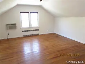 Additional living space featuring vaulted ceiling, dark wood-type flooring, radiator heating unit, and a wall mounted AC Additional living space featuring vaulted ceiling, dark wood-type flooring, radiator heating unit, and a wall mounted AC