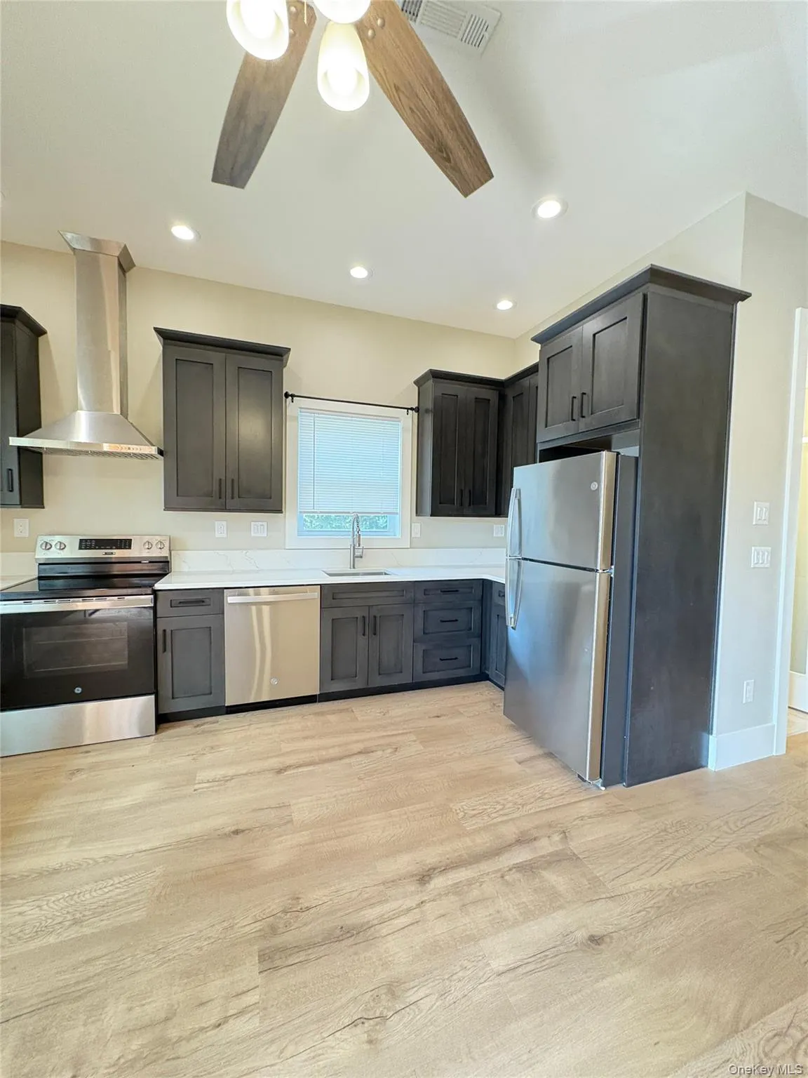 Kitchen featuring stainless steel appliances, wall chimney range hood, light wood-type flooring, recessed lighting, and a ceiling fan Kitchen featuring stainless steel appliances, wall chimney range hood, light wood-type flooring, recessed lighting, and a ceiling fan