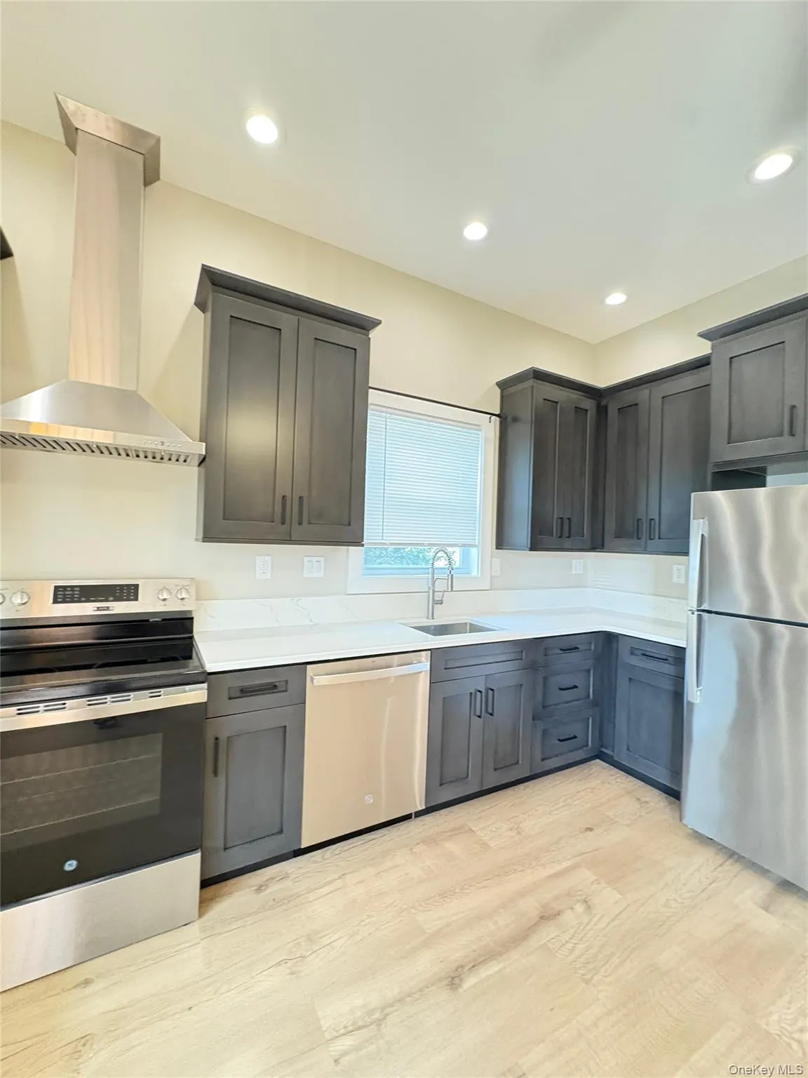Kitchen with appliances with stainless steel finishes, extractor fan, light wood-type flooring, recessed lighting, and light stone countertops Kitchen with appliances with stainless steel finishes, extractor fan, light wood-type flooring, recessed lighting, and light stone countertops