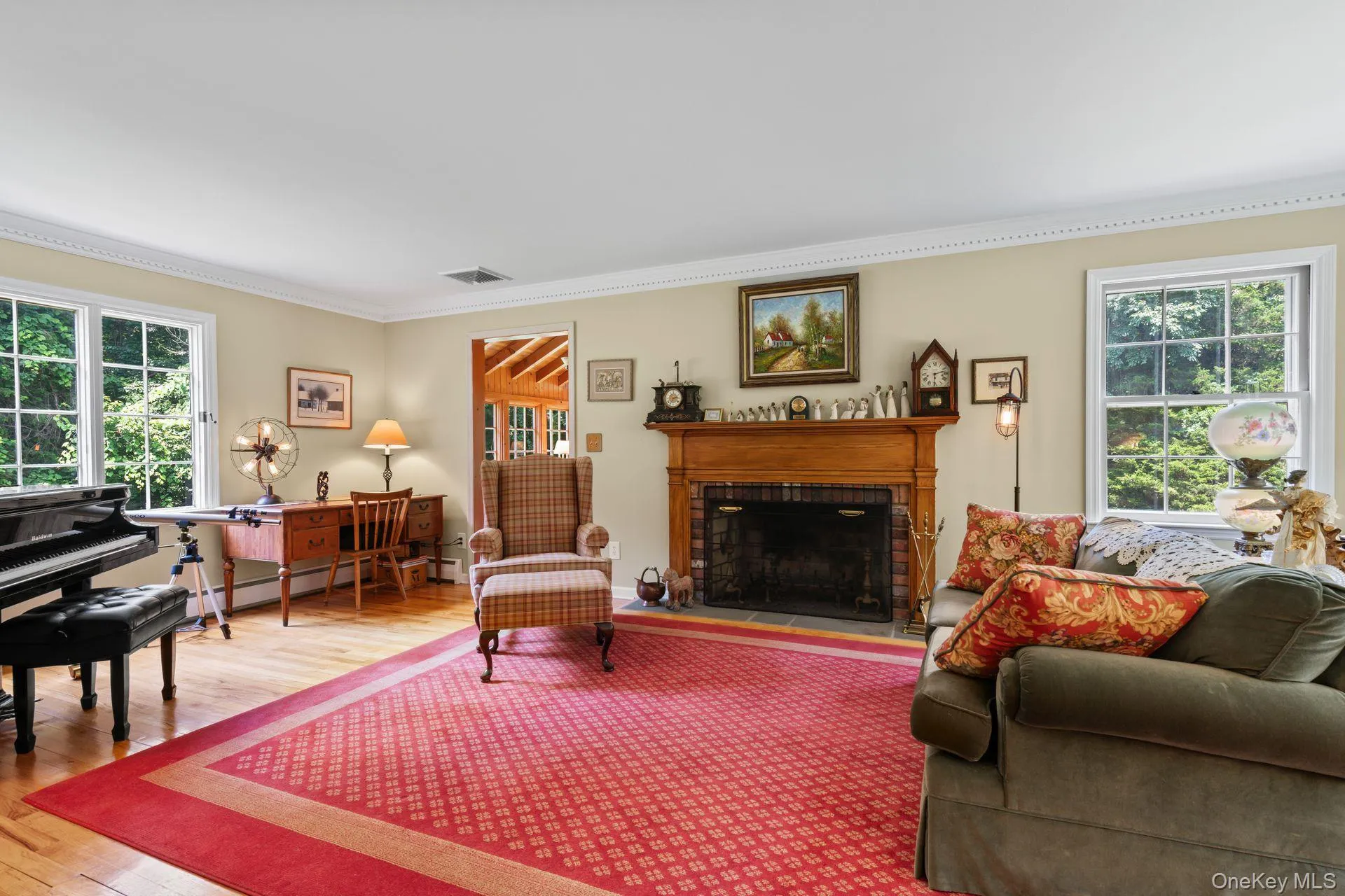 Living area featuring healthy amount of natural light, wood finished floors, a brick fireplace, ornamental molding, and a baseboard radiator Living area featuring healthy amount of natural light, wood finished floors, a brick fireplace, ornamental molding, and a baseboard radiator