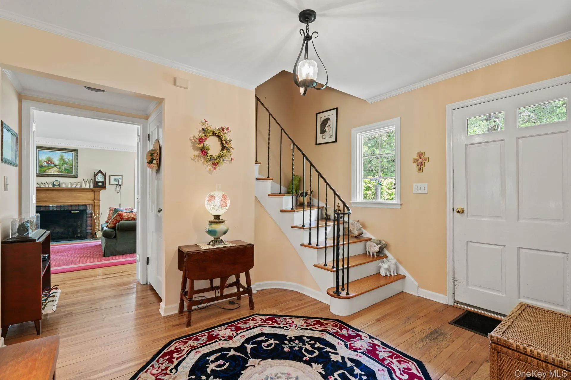 Entryway featuring light wood-style floors, crown molding, stairs, and a brick fireplace Entryway featuring light wood-style floors, crown molding, stairs, and a brick fireplace