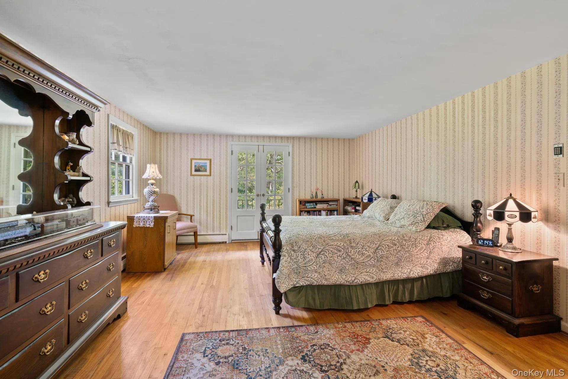 Bedroom with light wood-style floors, french doors, a baseboard heating unit, and wallpapered walls Bedroom with light wood-style floors, french doors, a baseboard heating unit, and wallpapered walls