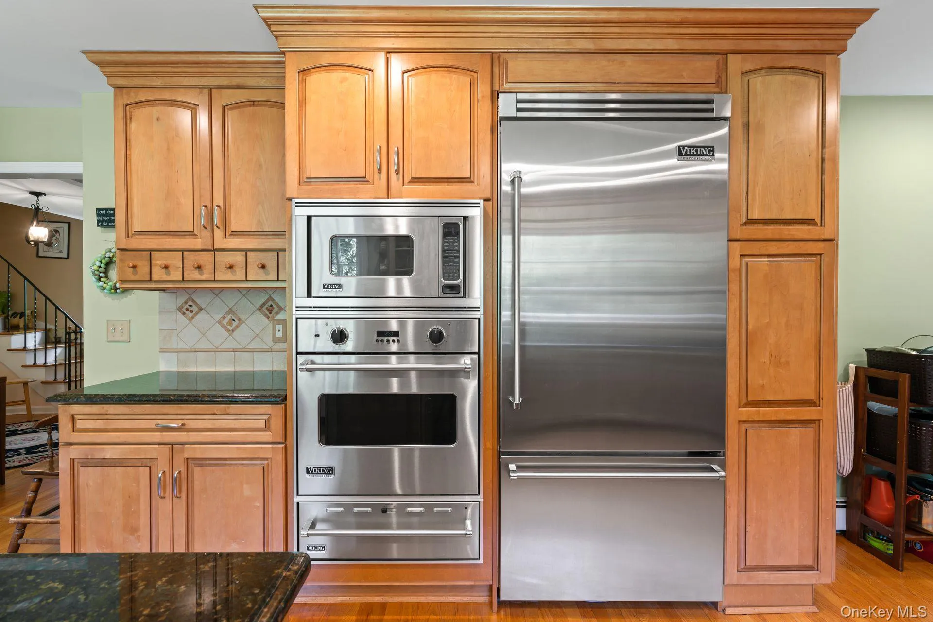 Kitchen with built in appliances, dark stone counters, a warming drawer, decorative backsplash, and light wood-style floors Kitchen with built in appliances, dark stone counters, a warming drawer, decorative backsplash, and light wood-style floors