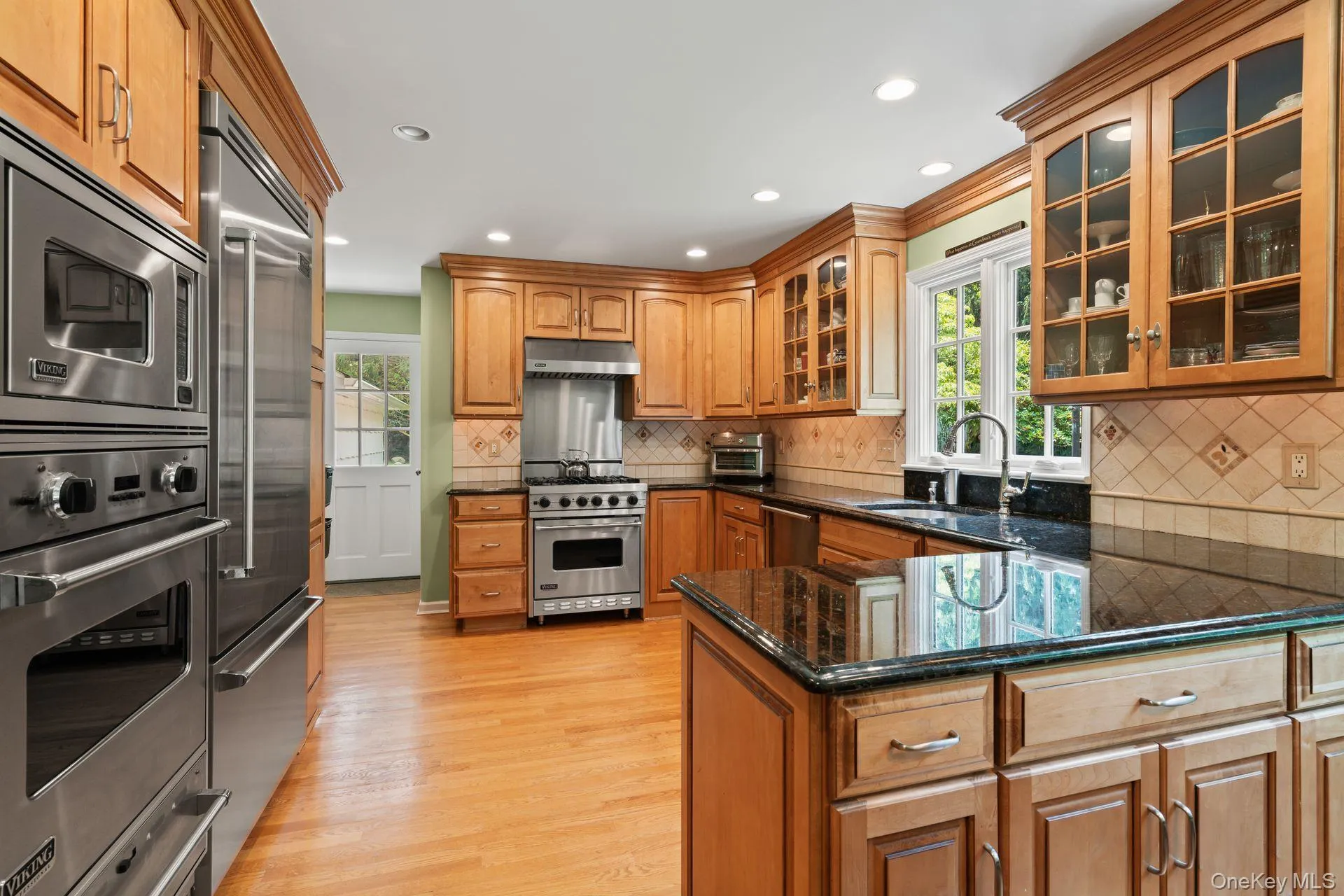 Kitchen with brown cabinets, built in appliances, dark stone countertops, glass insert cabinets, and recessed lighting Kitchen with brown cabinets, built in appliances, dark stone countertops, glass insert cabinets, and recessed lighting