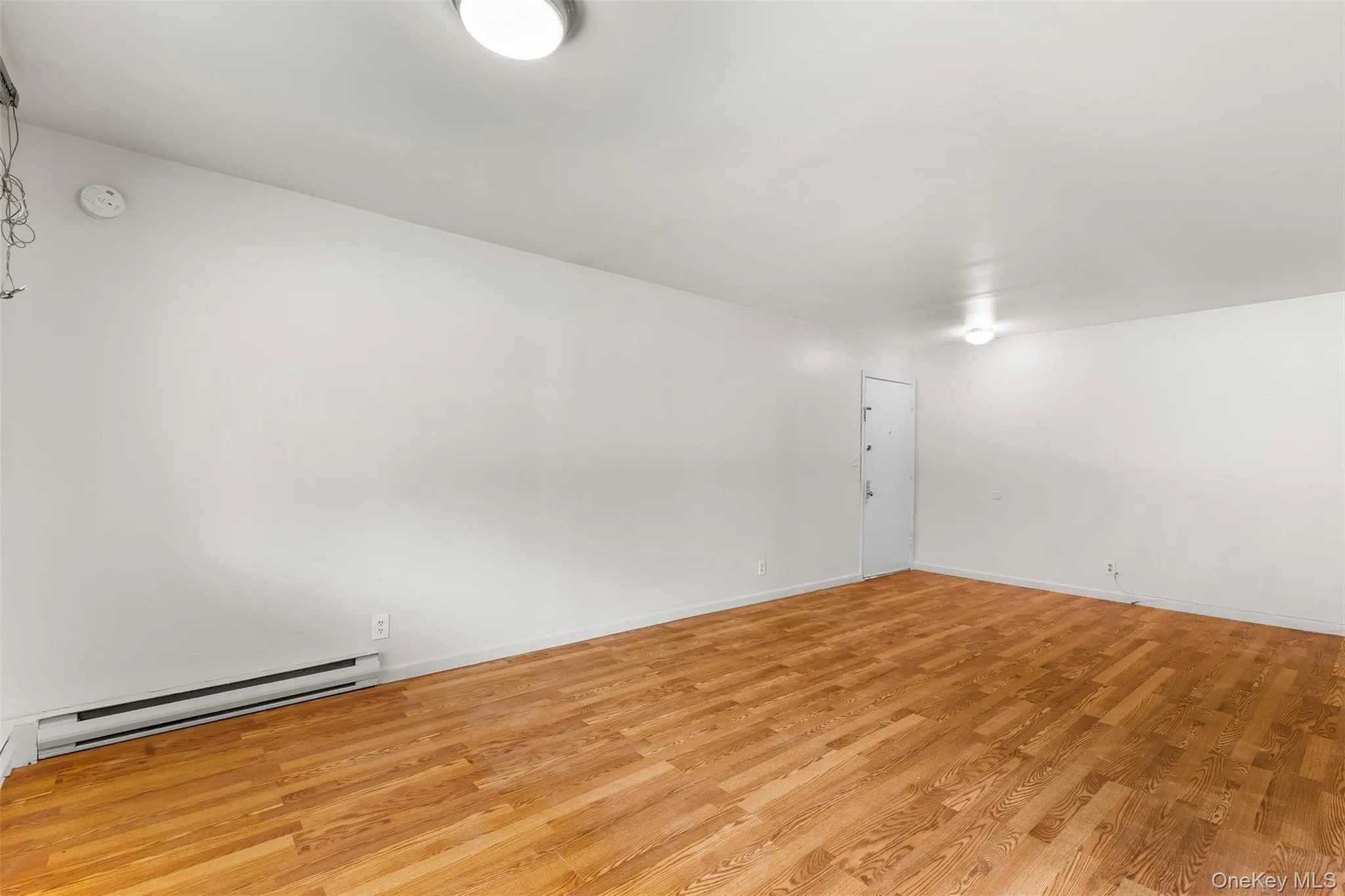 Empty room with light wood-type flooring and a baseboard heating unit Empty room with light wood-type flooring and a baseboard heating unit