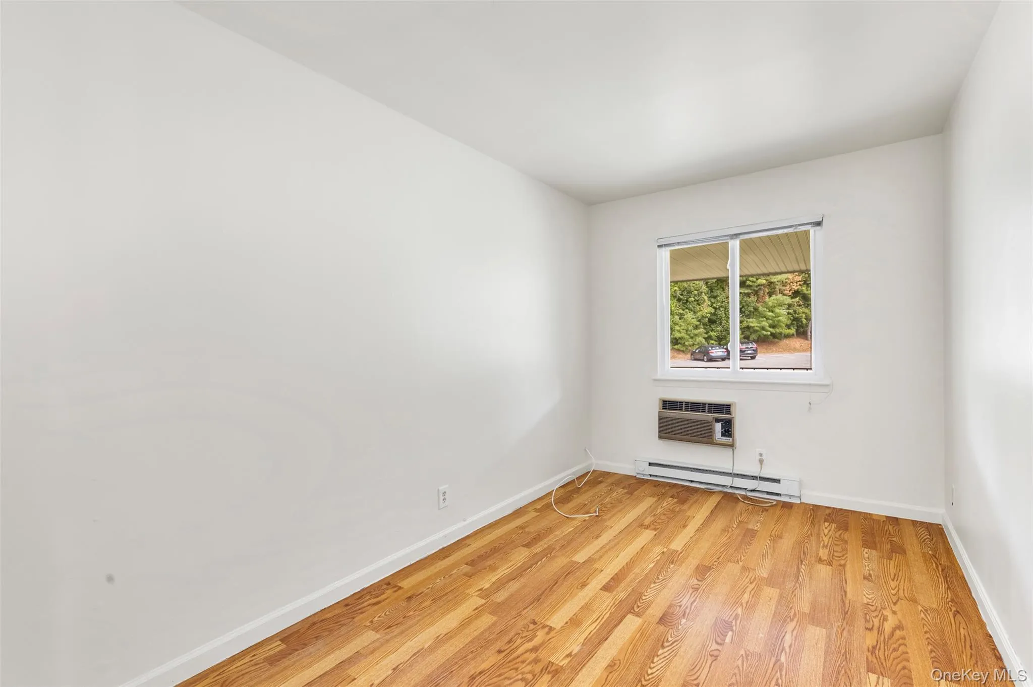 Bedroom featuring baseboard heating, light wood-type flooring, and a wall unit AC Bedroom featuring baseboard heating, light wood-type flooring, and a wall unit AC