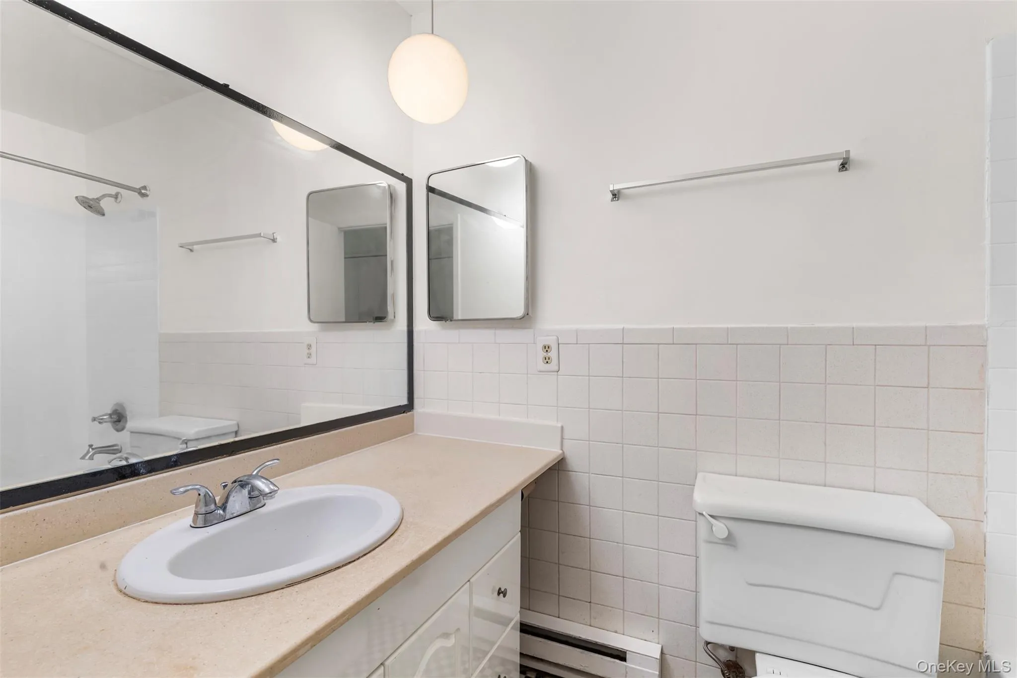Full bathroom with a baseboard radiator, tile walls, shower / tub combination, vanity, and a wainscoted wall Full bathroom with a baseboard radiator, tile walls, shower / tub combination, vanity, and a wainscoted wall