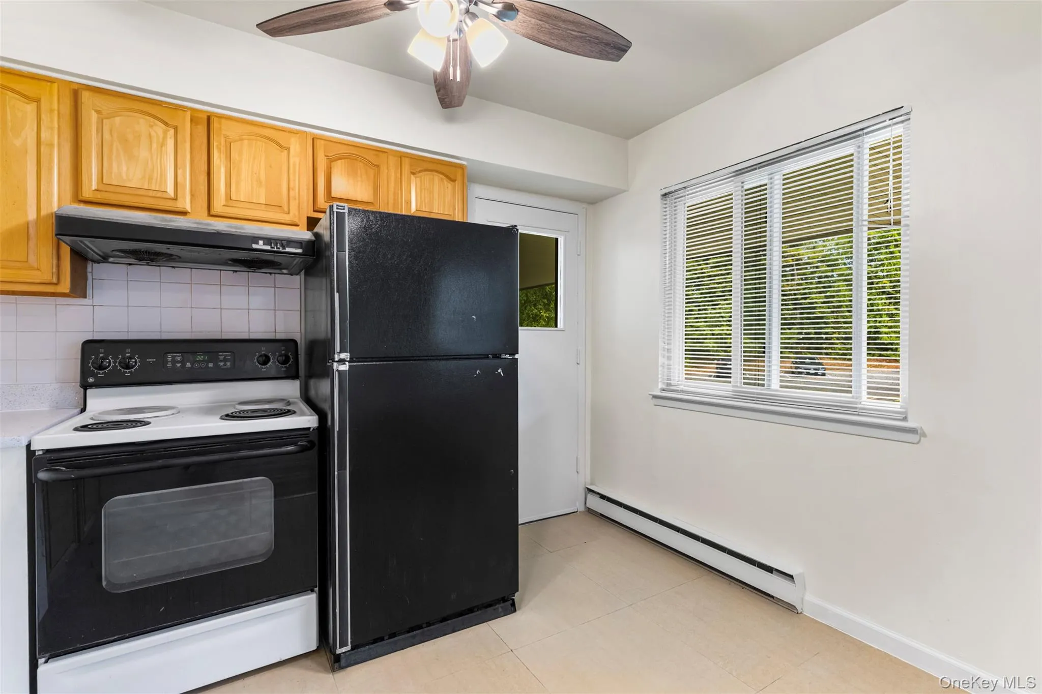 Kitchen with range with electric cooktop, freestanding refrigerator, baseboard heating, under cabinet range hood, and decorative backsplash Kitchen with range with electric cooktop, freestanding refrigerator, baseboard heating, under cabinet range hood, and decorative backsplash