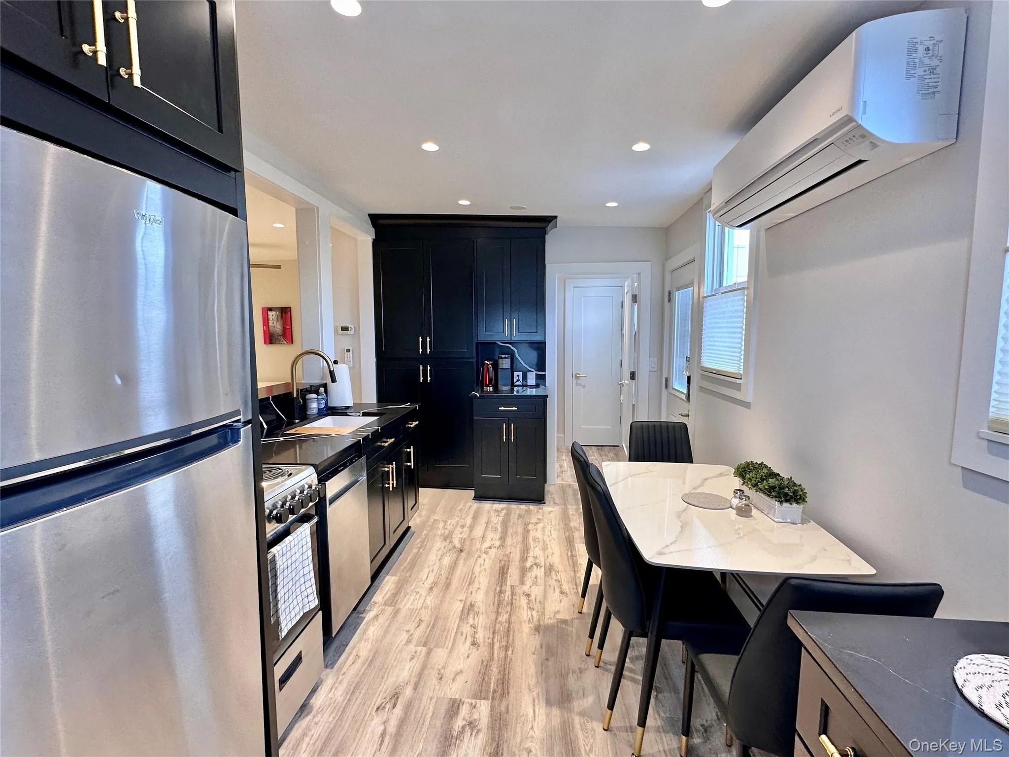 Kitchen with stainless steel appliances, dark cabinetry, an AC wall unit, light wood-style floors, and recessed lighting Kitchen with stainless steel appliances, dark cabinetry, an AC wall unit, light wood-style floors, and recessed lighting