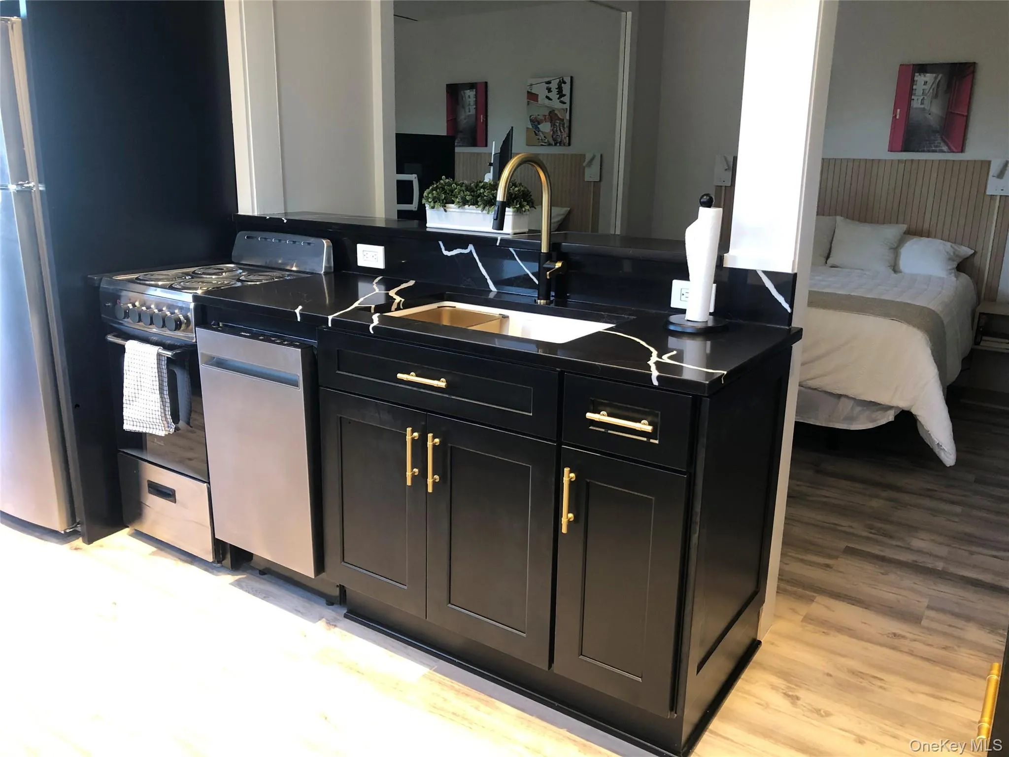Kitchen with dark cabinets, appliances with stainless steel finishes, light wood-style floors, and dark stone counters Kitchen with dark cabinets, appliances with stainless steel finishes, light wood-style floors, and dark stone counters