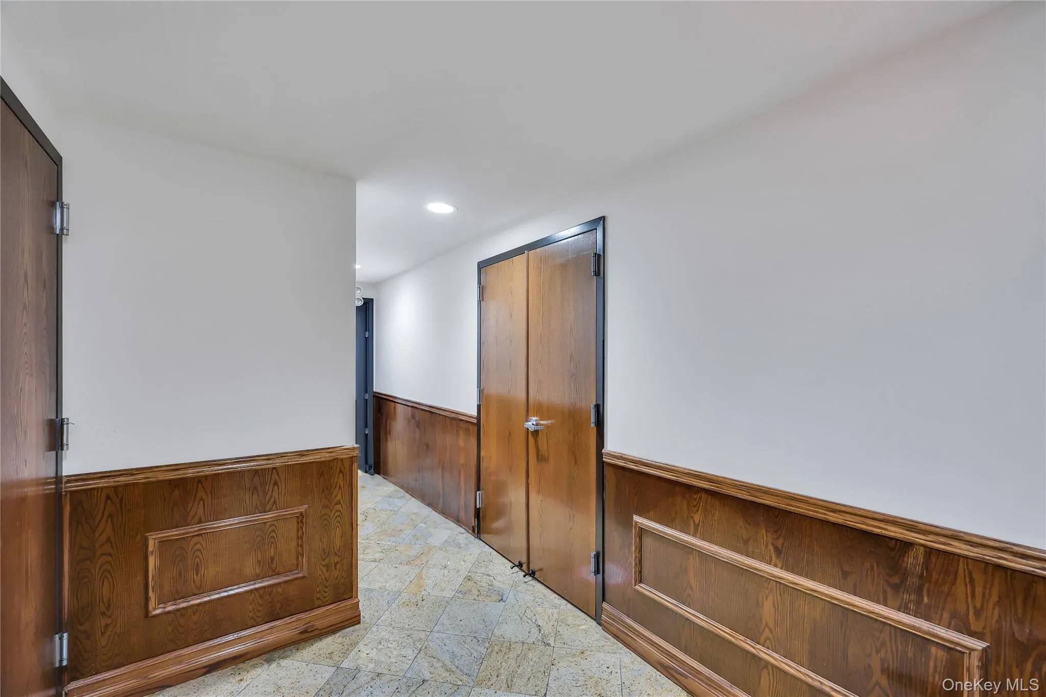 Hallway featuring a wainscoted wall, wooden walls, recessed lighting, and light stone finish flooring Hallway featuring a wainscoted wall, wooden walls, recessed lighting, and light stone finish flooring