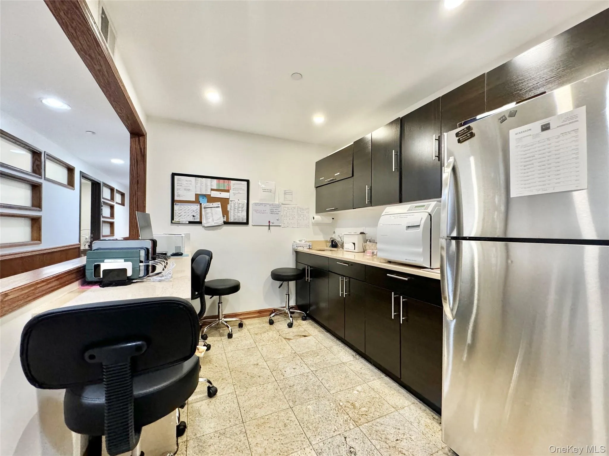 Kitchen featuring freestanding refrigerator, light countertops, a desk, recessed lighting, and dark cabinets Kitchen featuring freestanding refrigerator, light countertops, a desk, recessed lighting, and dark cabinets