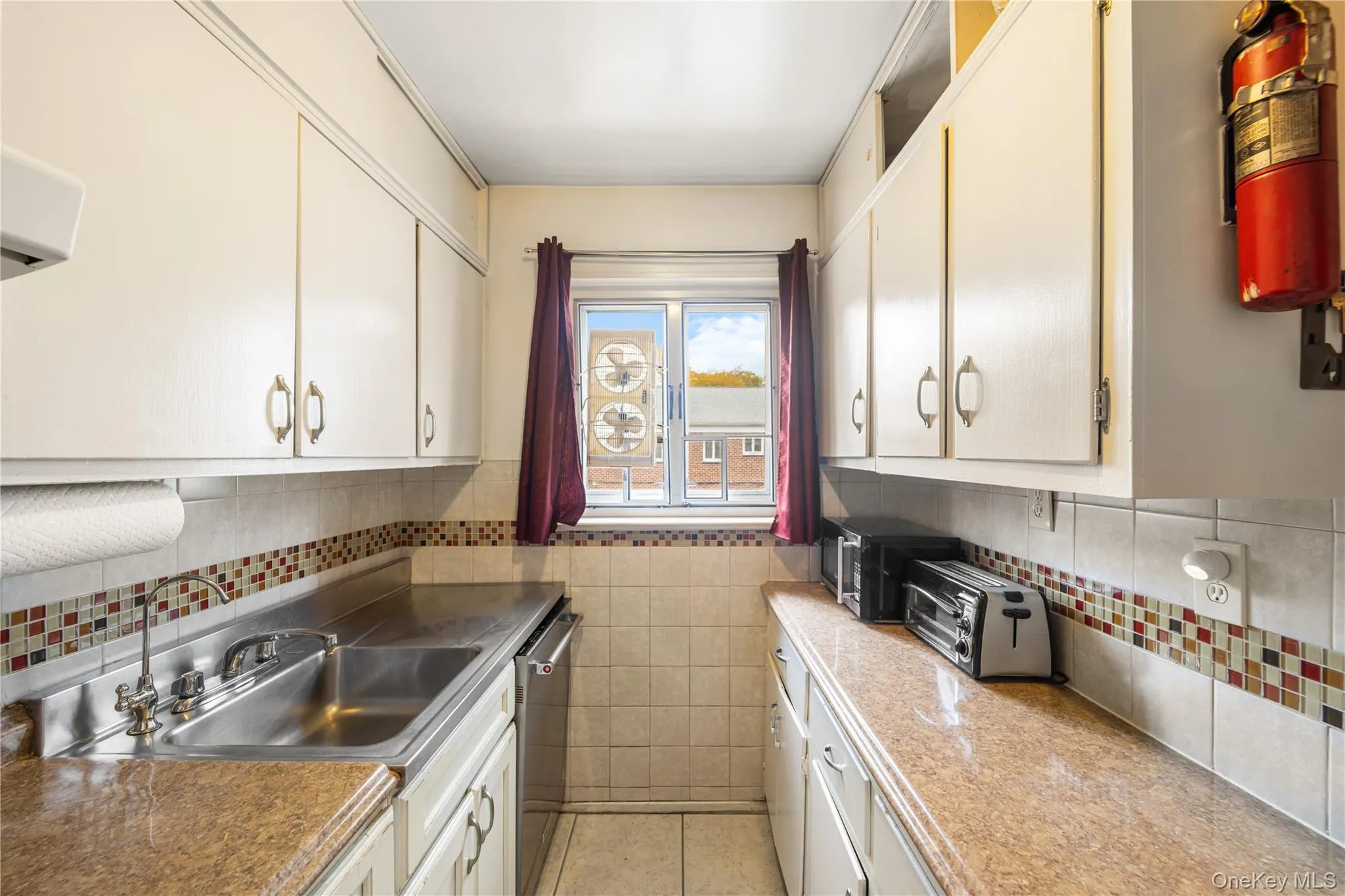 Kitchen featuring light tile patterned flooring, dishwasher, white cabinets, tile walls, and decorative backsplash Kitchen featuring light tile patterned flooring, dishwasher, white cabinets, tile walls, and decorative backsplash