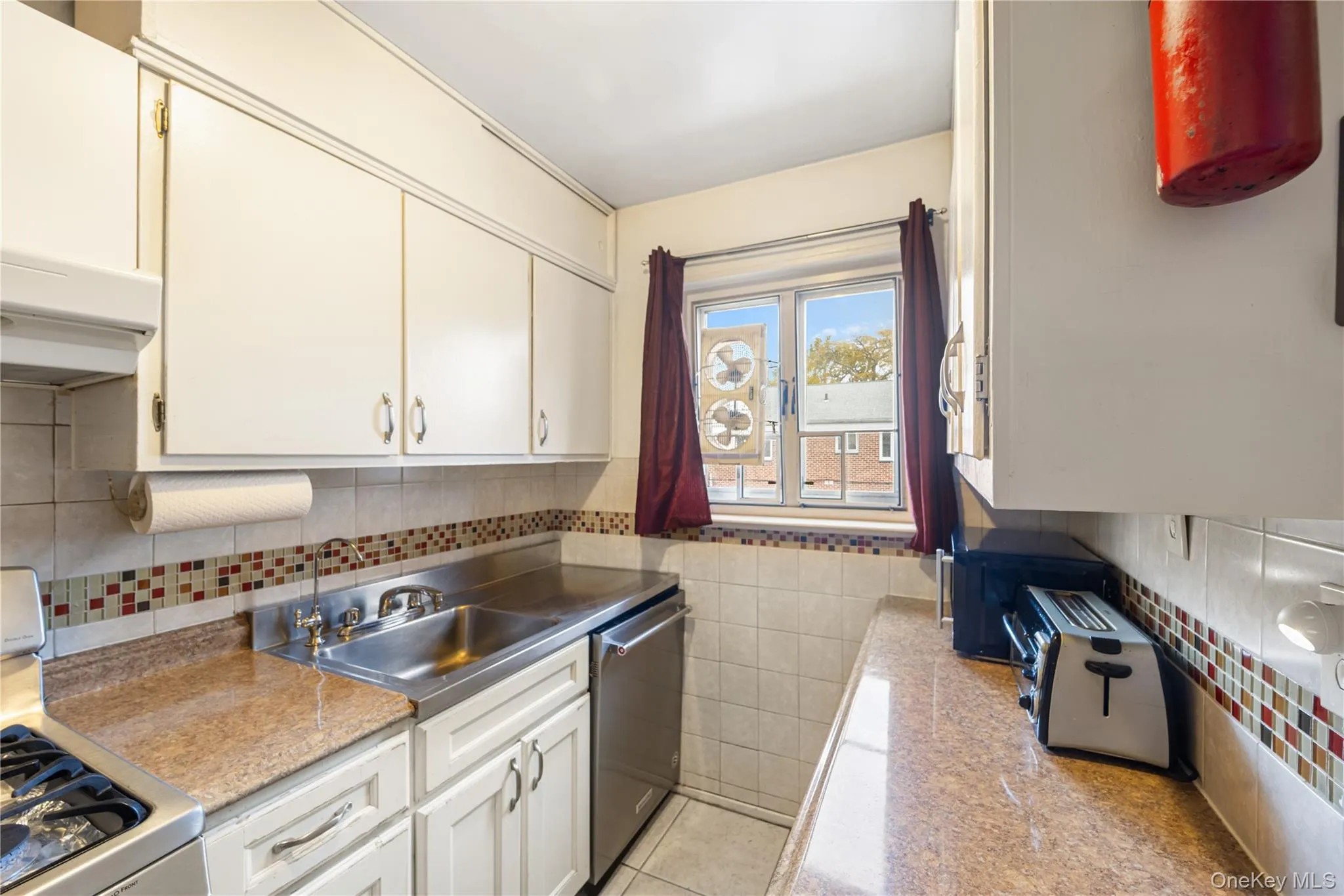 Kitchen featuring appliances with stainless steel finishes, light tile patterned floors, extractor fan, white cabinets, and decorative backsplash Kitchen featuring appliances with stainless steel finishes, light tile patterned floors, extractor fan, white cabinets, and decorative backsplash