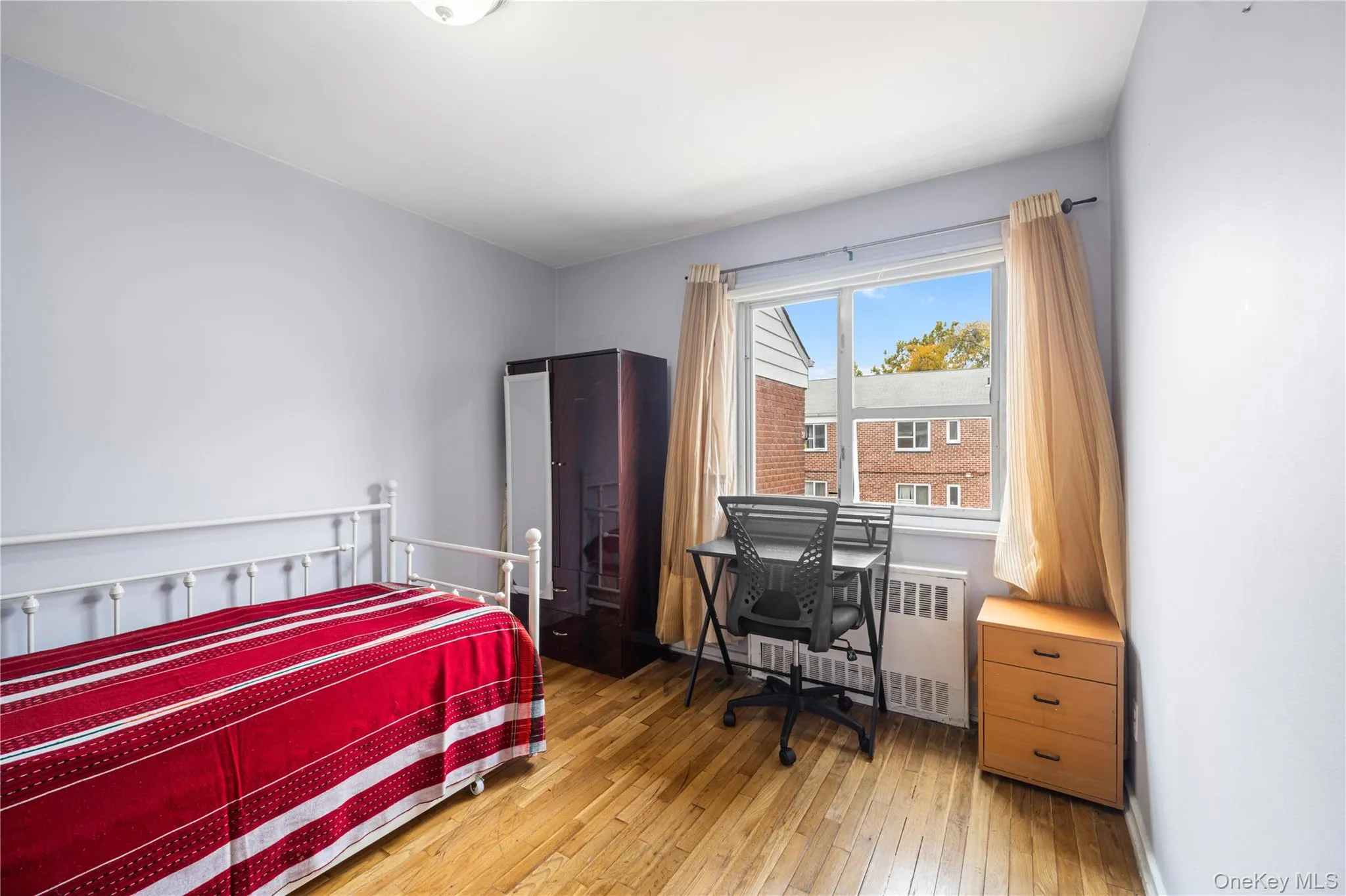 Bedroom featuring light wood finished floors, radiator, and an office area Bedroom featuring light wood finished floors, radiator, and an office area