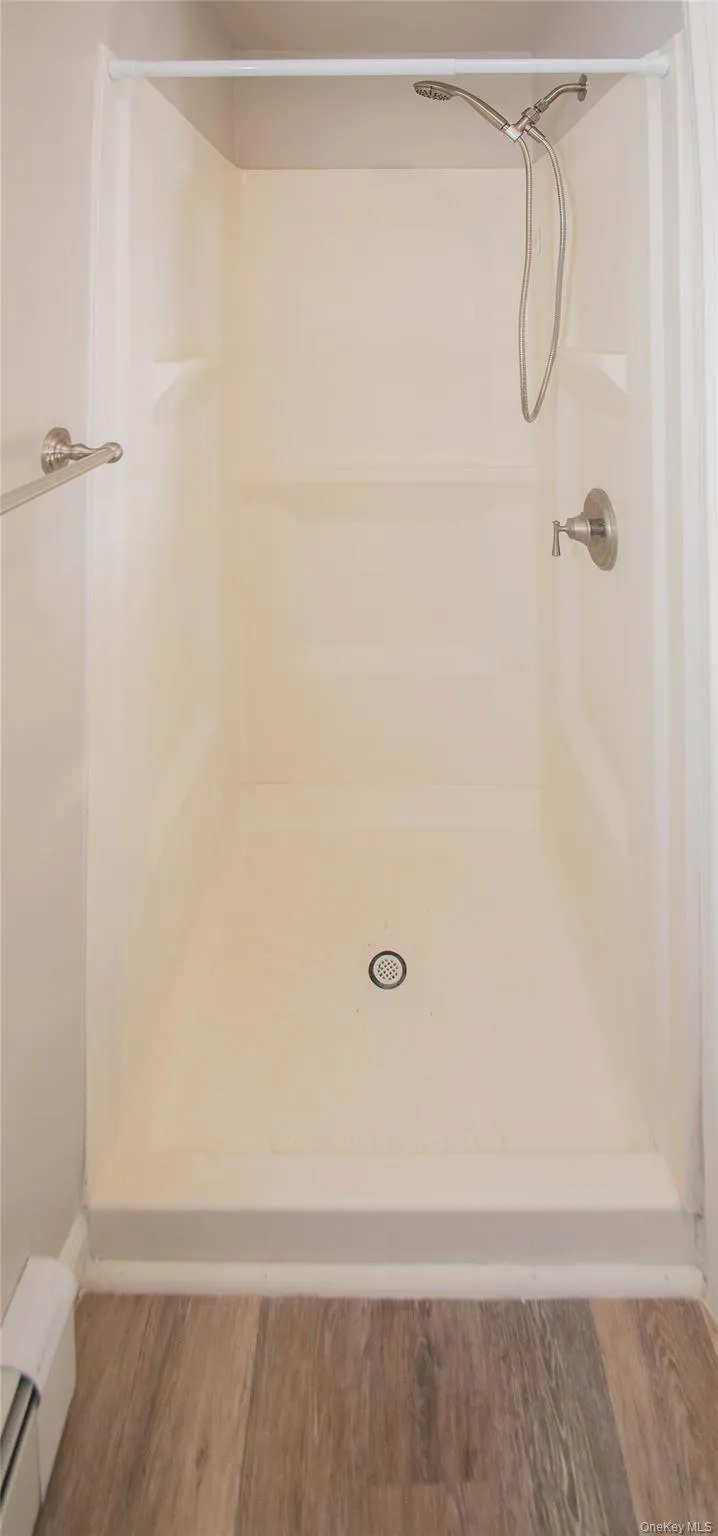 Bathroom with a shower stall, baseboard heating, and wood finished floors Bathroom with a shower stall, baseboard heating, and wood finished floors