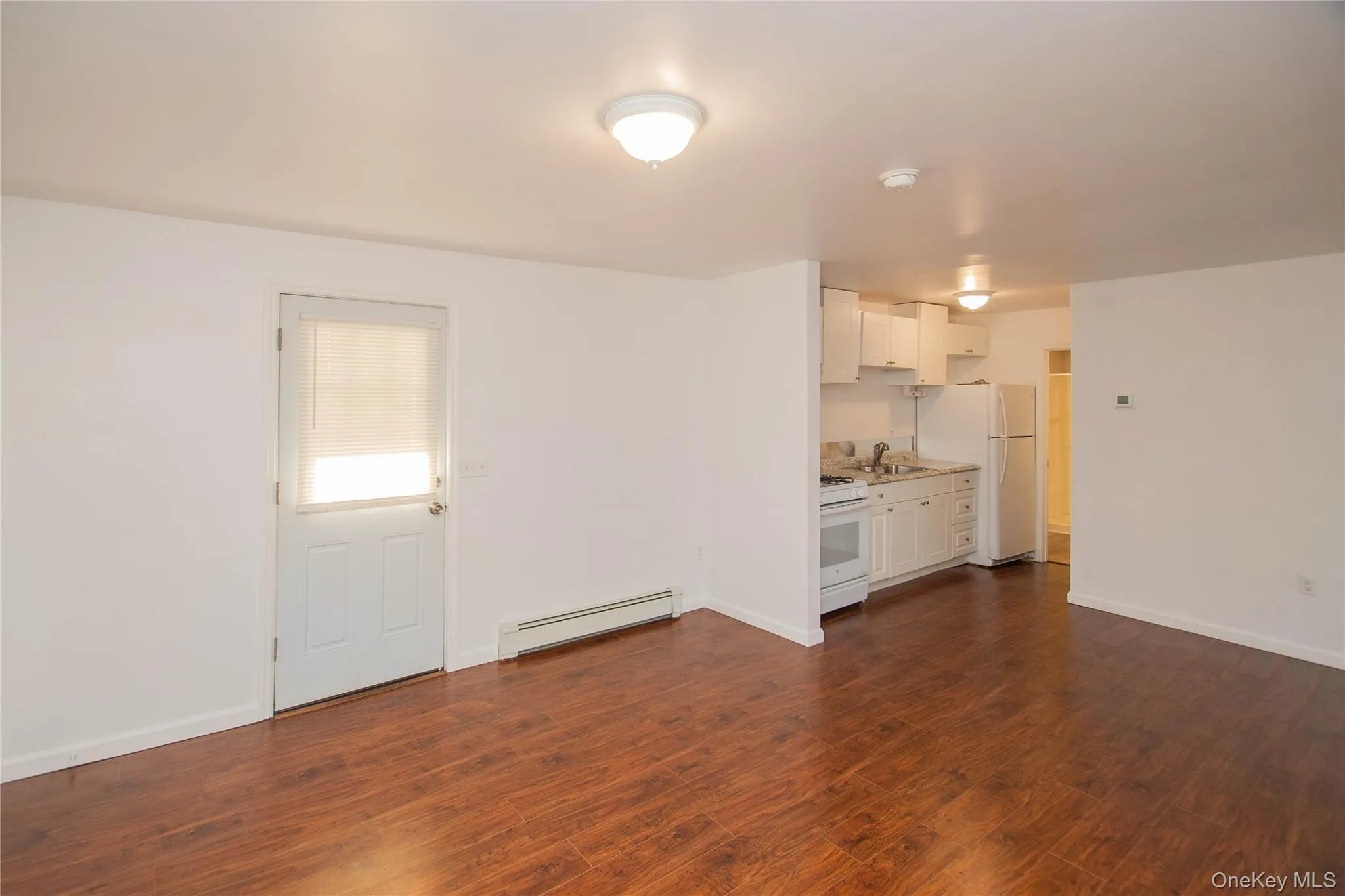 Unfurnished living room with baseboard heating and dark wood-type flooring Unfurnished living room with baseboard heating and dark wood-type flooring