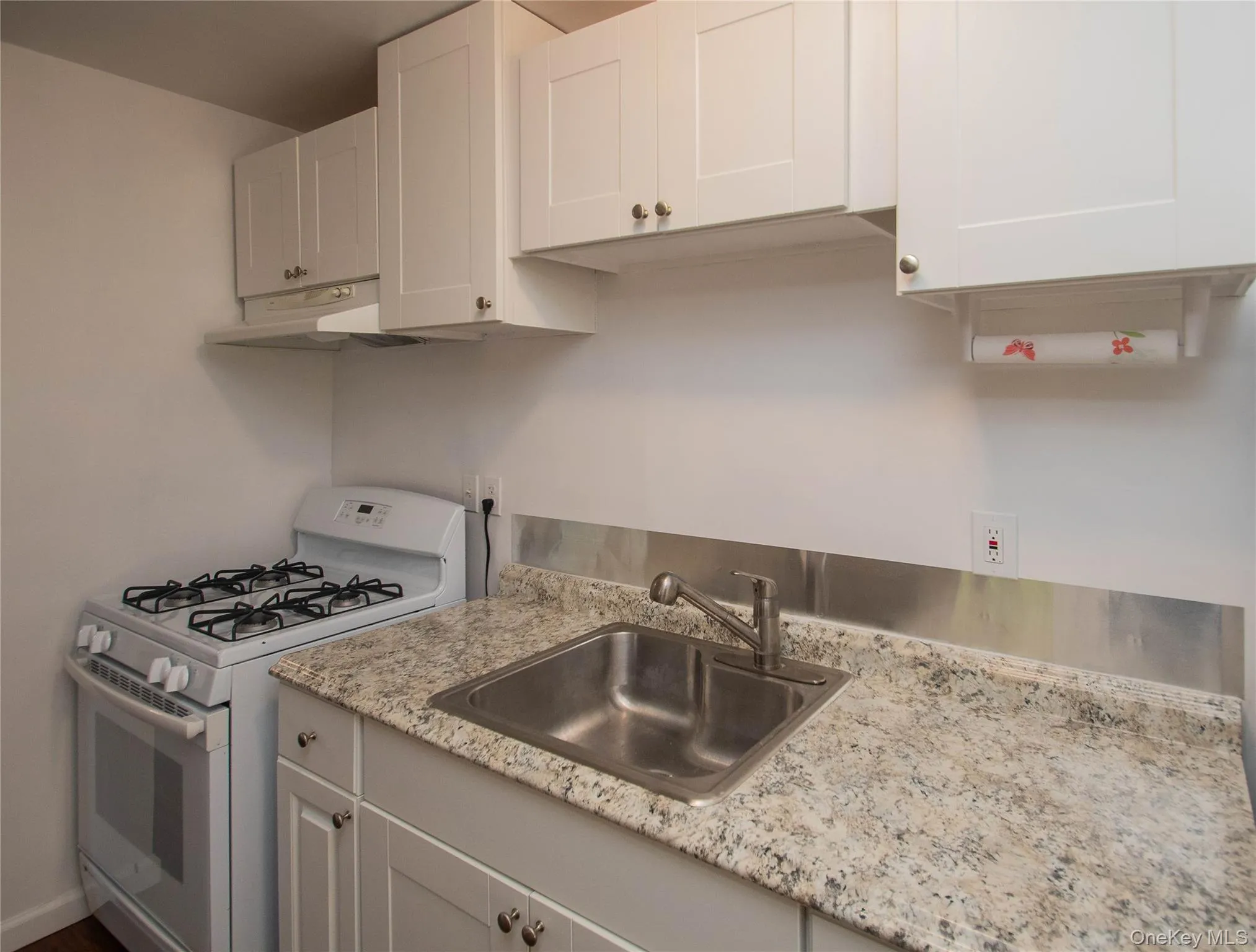 Kitchen featuring white gas range oven, white cabinetry, under cabinet range hood, and light stone countertops Kitchen featuring white gas range oven, white cabinetry, under cabinet range hood, and light stone countertops