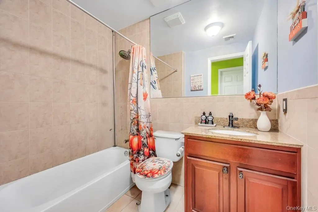 Bathroom with shower / bath combination with curtain, tile walls, vanity, and light tile patterned floors Bathroom with shower / bath combination with curtain, tile walls, vanity, and light tile patterned floors