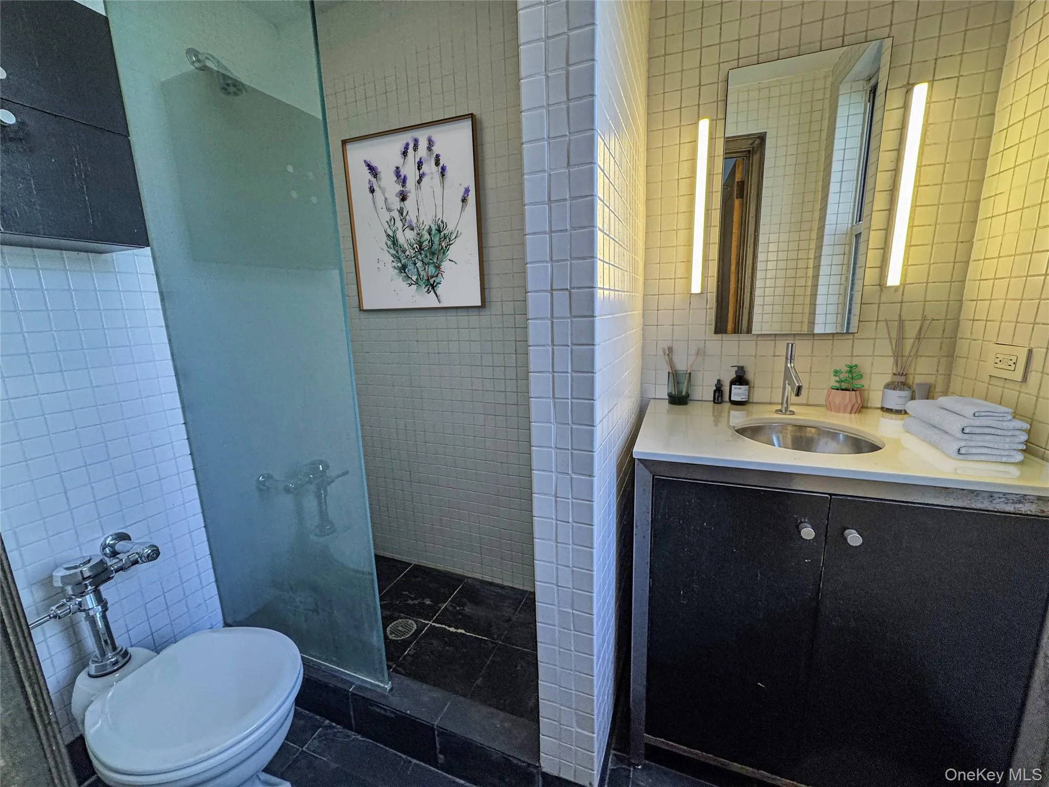 Full bath featuring tile walls, vanity, tiled shower, and dark tile patterned flooring Full bath featuring tile walls, vanity, tiled shower, and dark tile patterned flooring