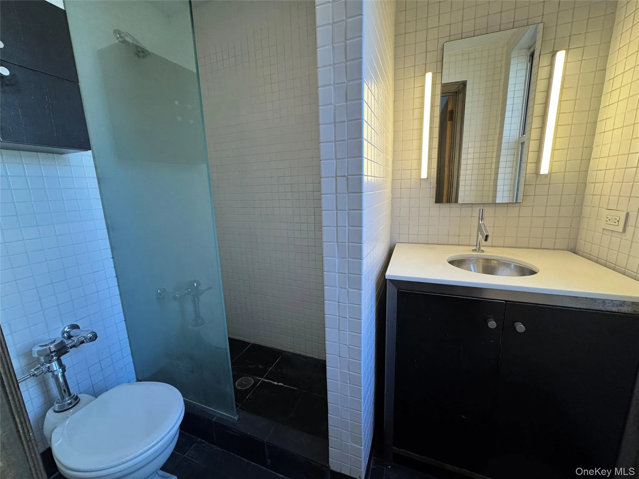 Bathroom featuring tile walls, tiled shower, vanity, and dark tile patterned flooring Bathroom featuring tile walls, tiled shower, vanity, and dark tile patterned flooring