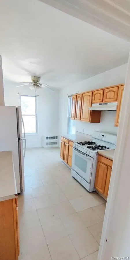 Kitchen featuring white appliances, light countertops, under cabinet range hood, and ceiling fan Kitchen featuring white appliances, light countertops, under cabinet range hood, and ceiling fan