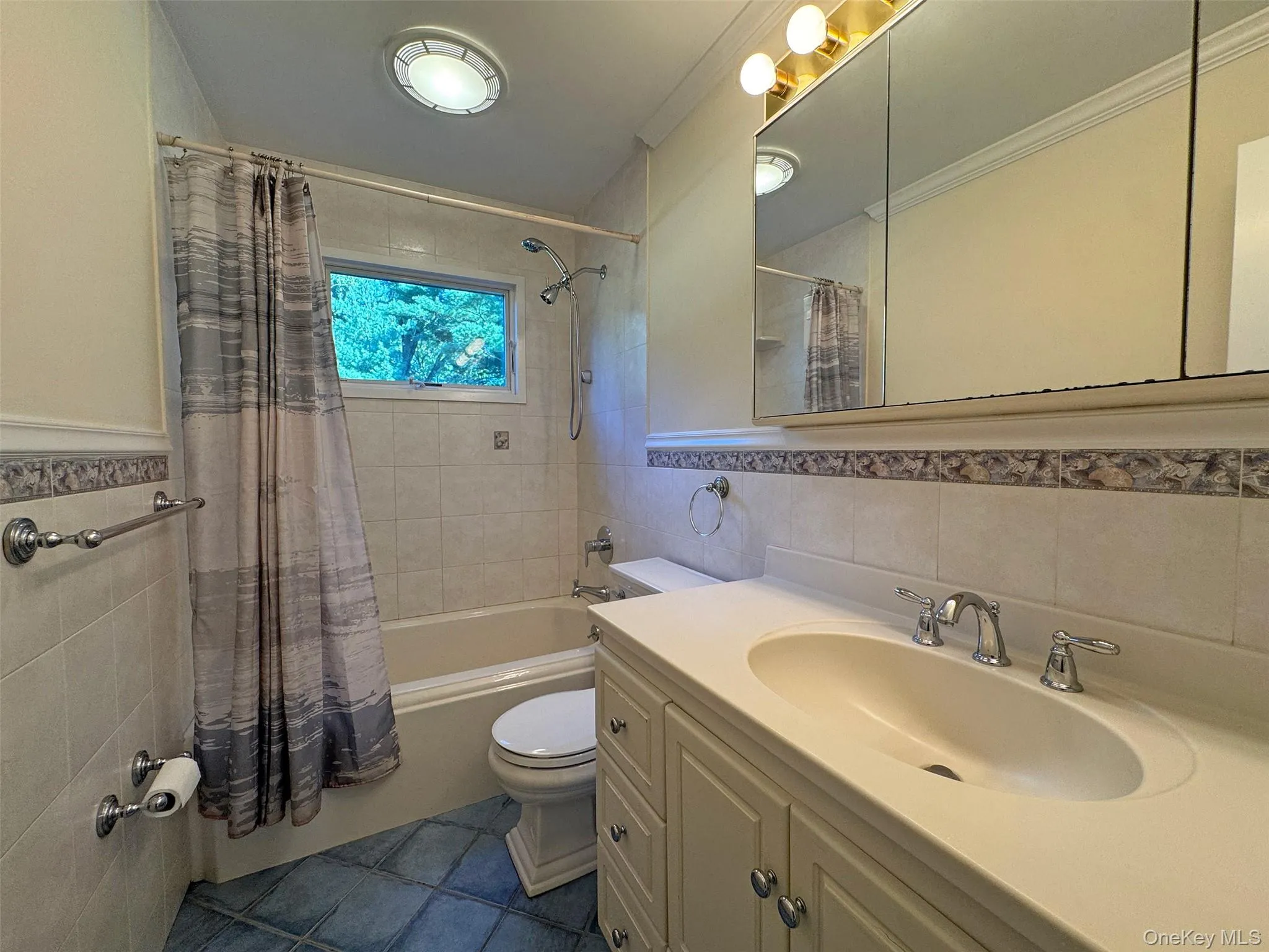 Full bathroom with tile walls, shower / bath combo with shower curtain, vanity, ornamental molding, and dark tile patterned floors Full bathroom with tile walls, shower / bath combo with shower curtain, vanity, ornamental molding, and dark tile patterned floors