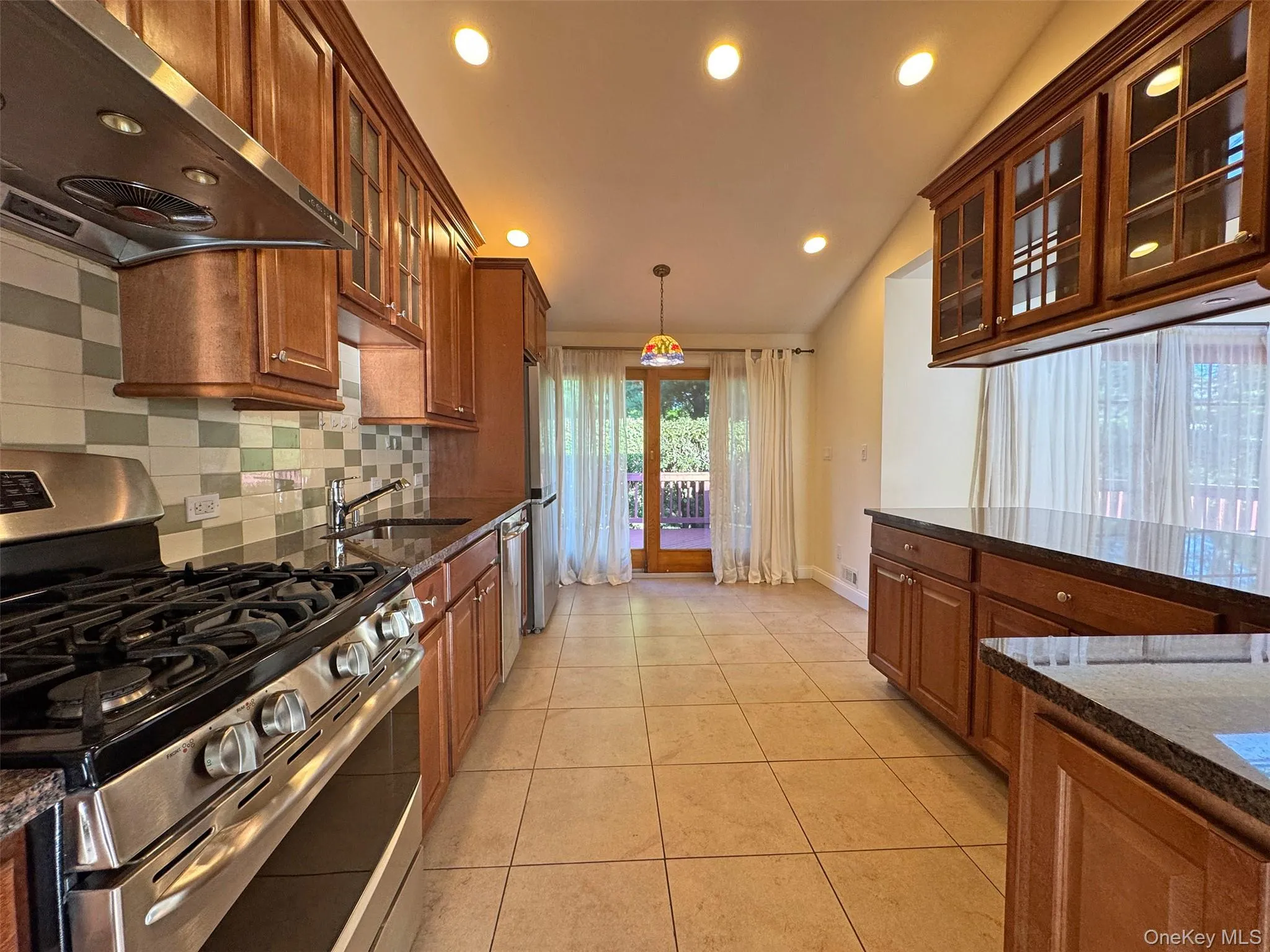 Kitchen featuring glass insert cabinets, stainless steel appliances, extractor fan, tasteful backsplash, and decorative light fixtures Kitchen featuring glass insert cabinets, stainless steel appliances, extractor fan, tasteful backsplash, and decorative light fixtures