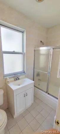 Full bathroom featuring enclosed tub / shower combo, vanity, and light tile patterned flooring Full bathroom featuring enclosed tub / shower combo, vanity, and light tile patterned flooring