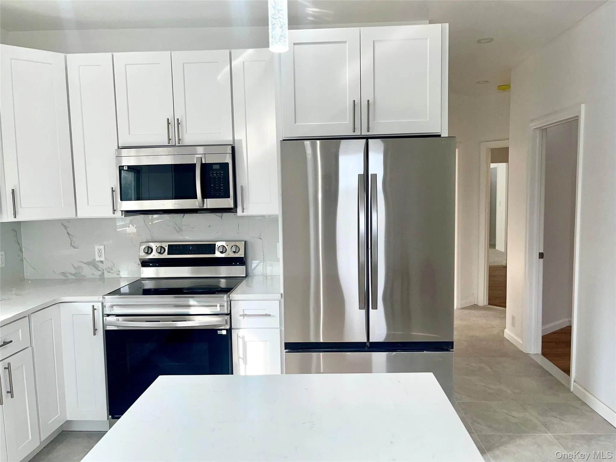 Kitchen featuring stainless steel appliances, white cabinets, light stone counters, and backsplash Kitchen featuring stainless steel appliances, white cabinets, light stone counters, and backsplash