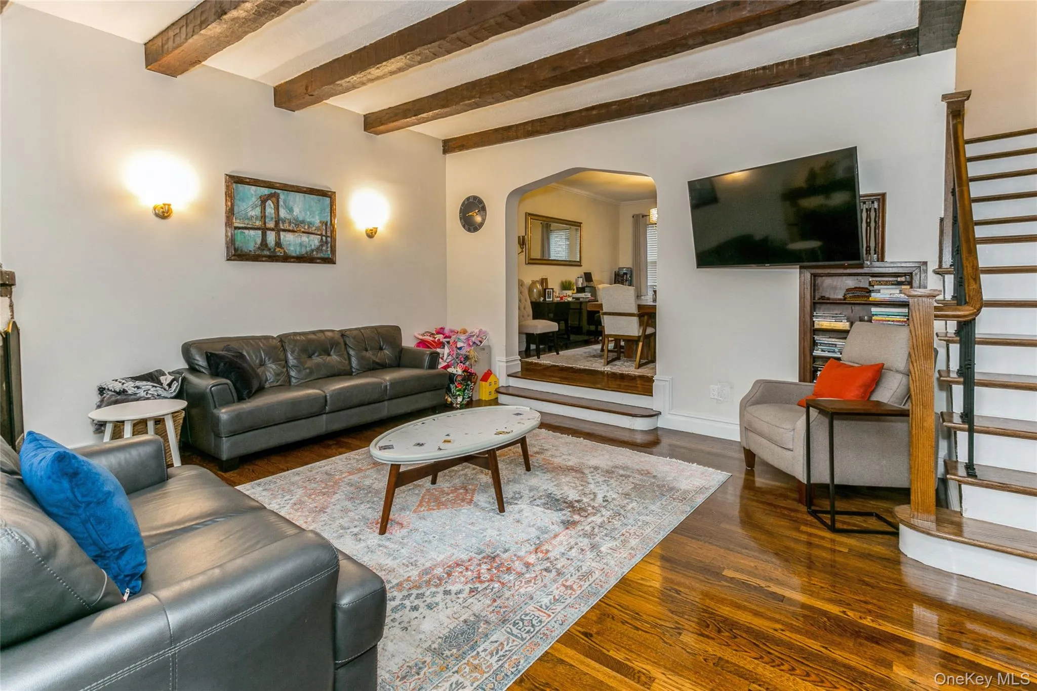 Living area with stairs, arched walkways, dark wood-style flooring, and beamed ceiling Living area with stairs, arched walkways, dark wood-style flooring, and beamed ceiling