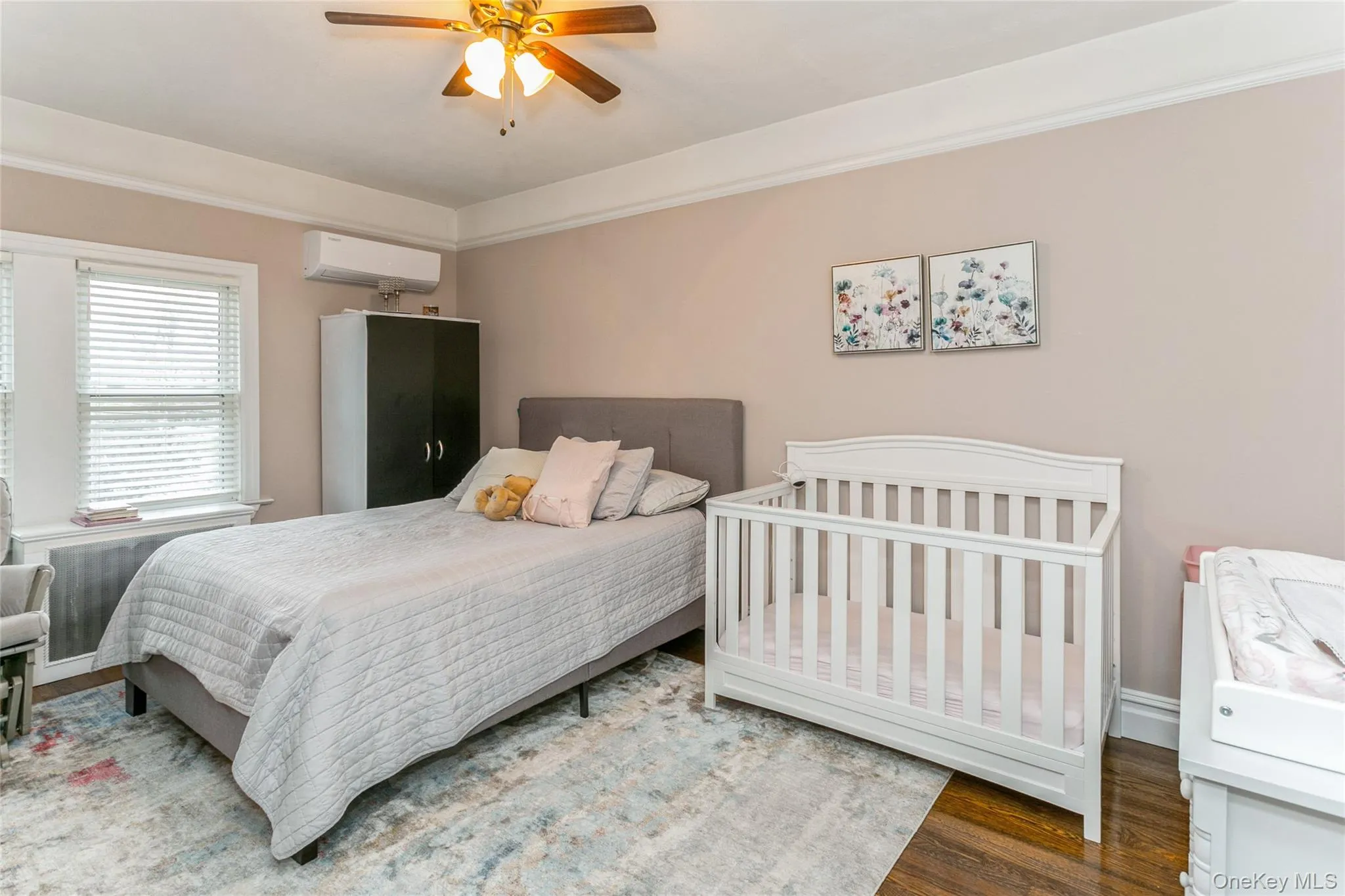 Bedroom featuring wood finished floors, ceiling fan, a wall unit AC, crown molding, and radiator heating unit Bedroom featuring wood finished floors, ceiling fan, a wall unit AC, crown molding, and radiator heating unit