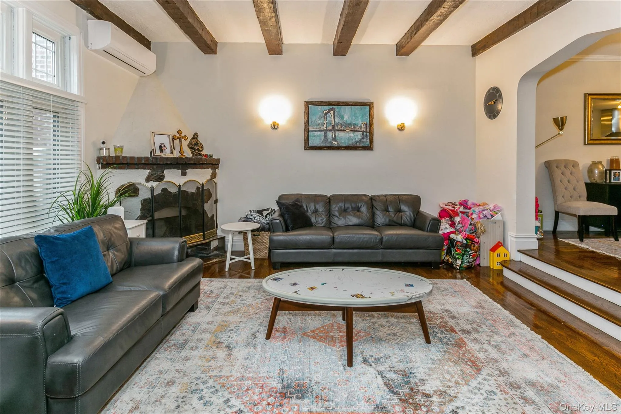 Living area with wood finished floors, arched walkways, a fireplace, a wall unit AC, and beamed ceiling Living area with wood finished floors, arched walkways, a fireplace, a wall unit AC, and beamed ceiling