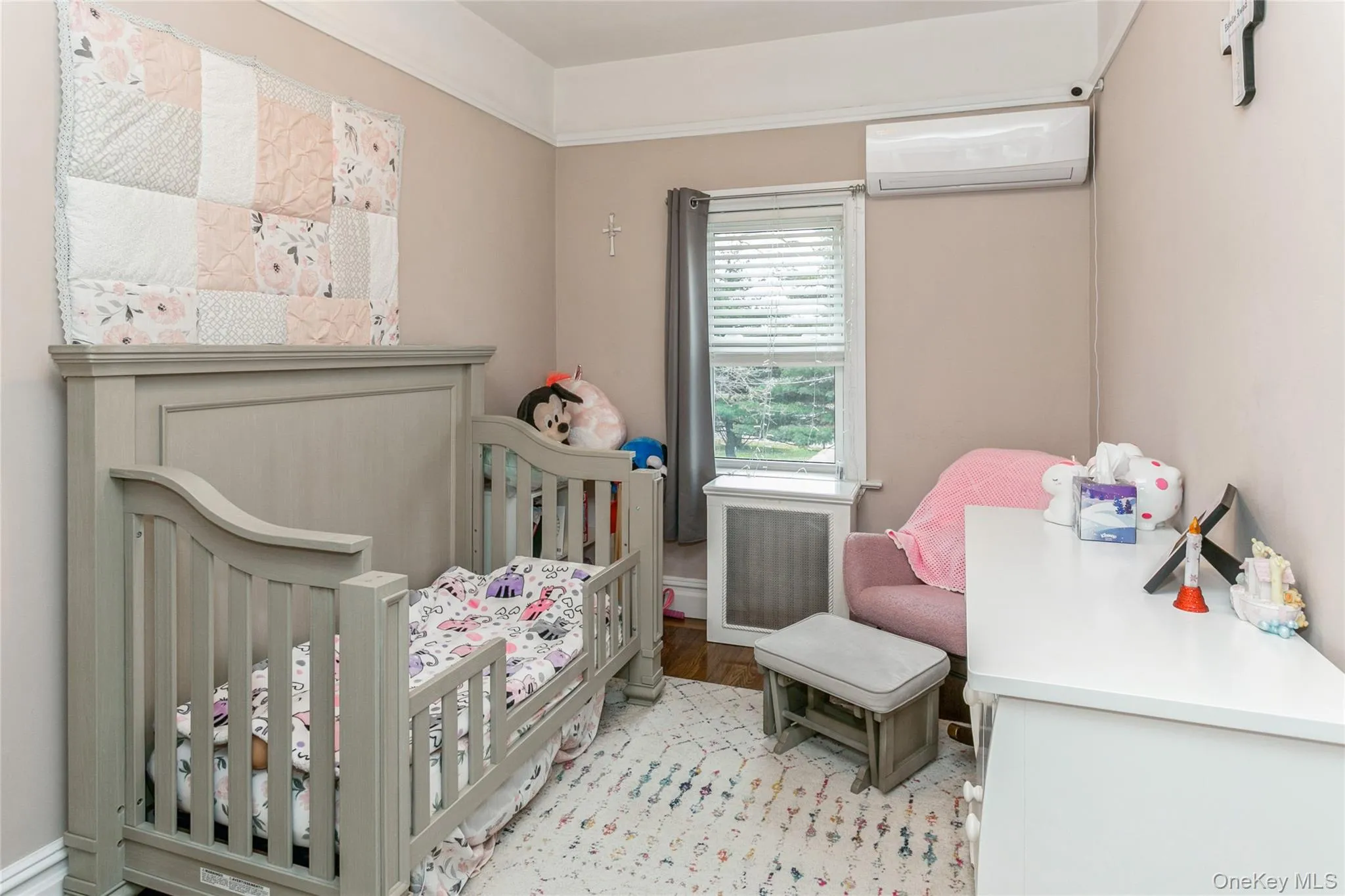 Bedroom featuring a nursery area, radiator, a wall unit AC, and light wood finished floors Bedroom featuring a nursery area, radiator, a wall unit AC, and light wood finished floors