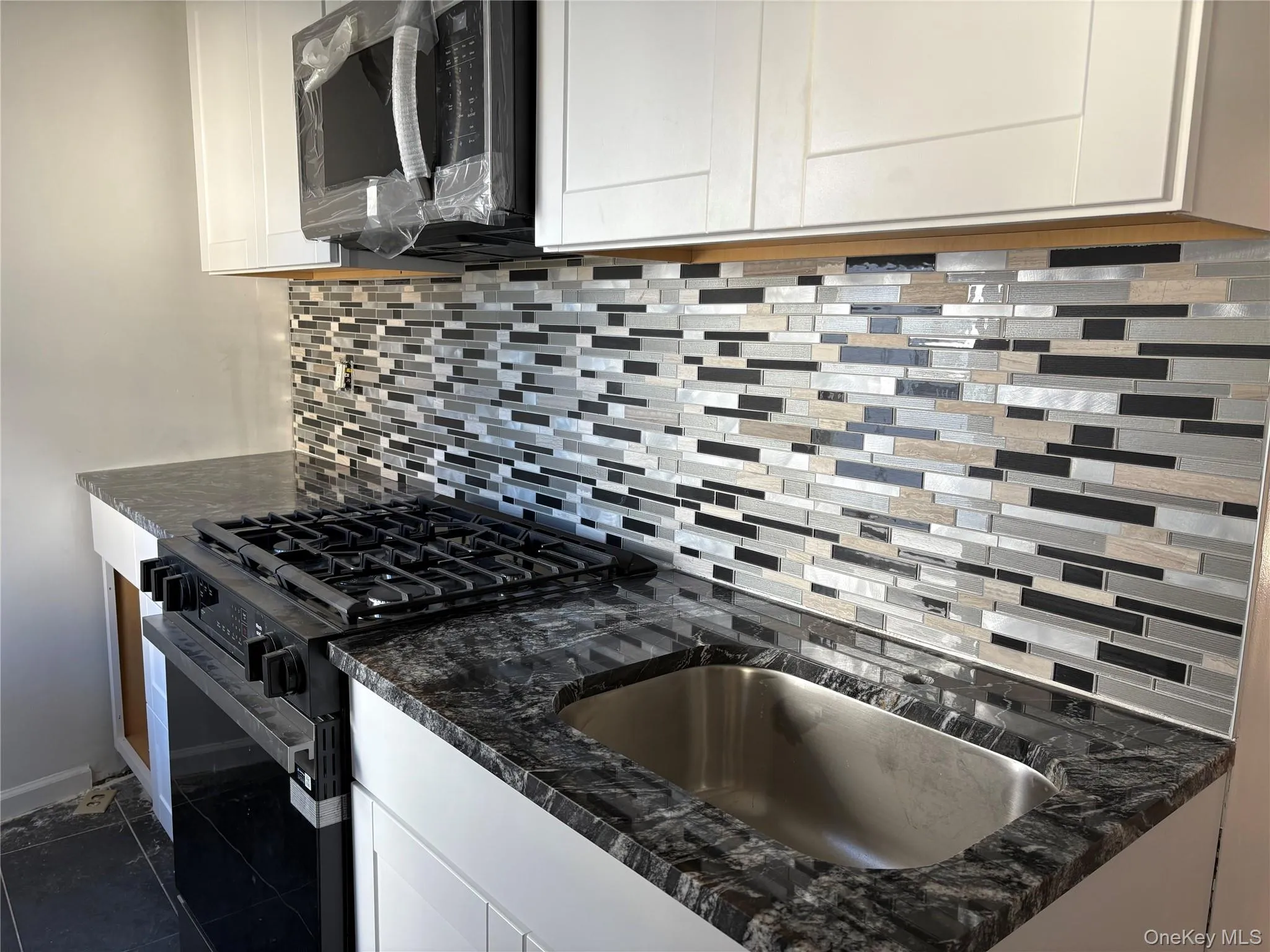 New Kitchen featuring tasteful backsplash, gas stove, white cabinetry, dark stone counters, and dark tile patterned flooring New Kitchen featuring tasteful backsplash, gas stove, white cabinetry, dark stone counters, and dark tile patterned flooring