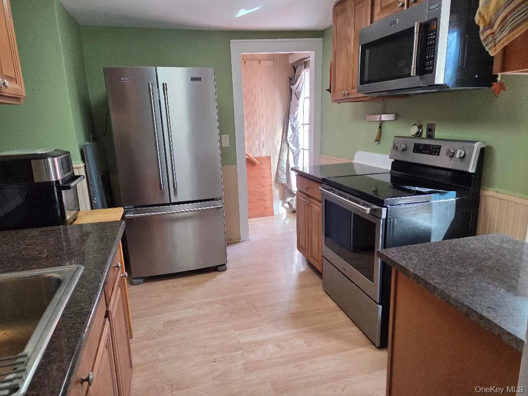 Kitchen featuring stainless steel appliances, light wood-type flooring, brown cabinets, and a wainscoted wall Kitchen featuring stainless steel appliances, light wood-type flooring, brown cabinets, and a wainscoted wall