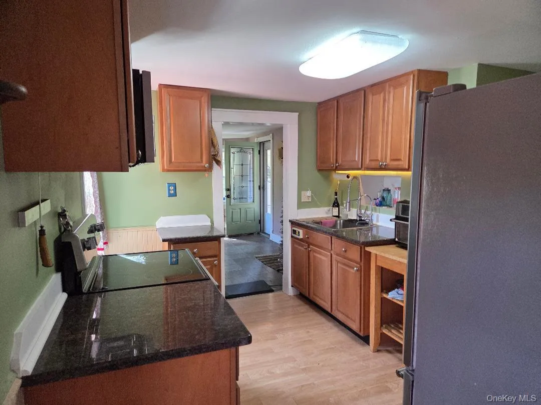 Kitchen with black appliances, dark stone countertops, brown cabinetry, and light wood finished floors Kitchen with black appliances, dark stone countertops, brown cabinetry, and light wood finished floors