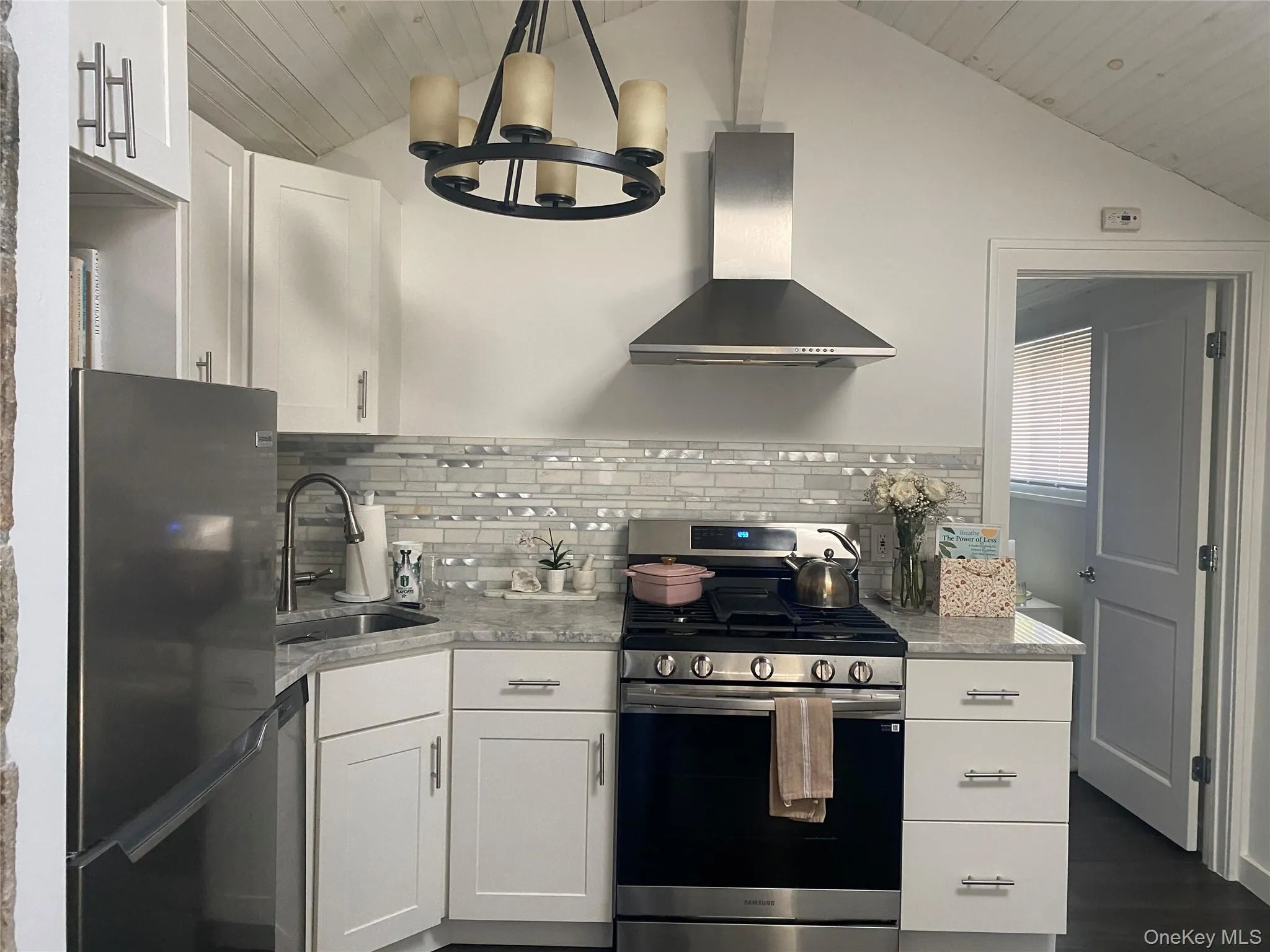 Kitchen with appliances with stainless steel finishes, white cabinetry, wall chimney exhaust hood, vaulted ceiling, and tasteful backsplash Kitchen with appliances with stainless steel finishes, white cabinetry, wall chimney exhaust hood, vaulted ceiling, and tasteful backsplash