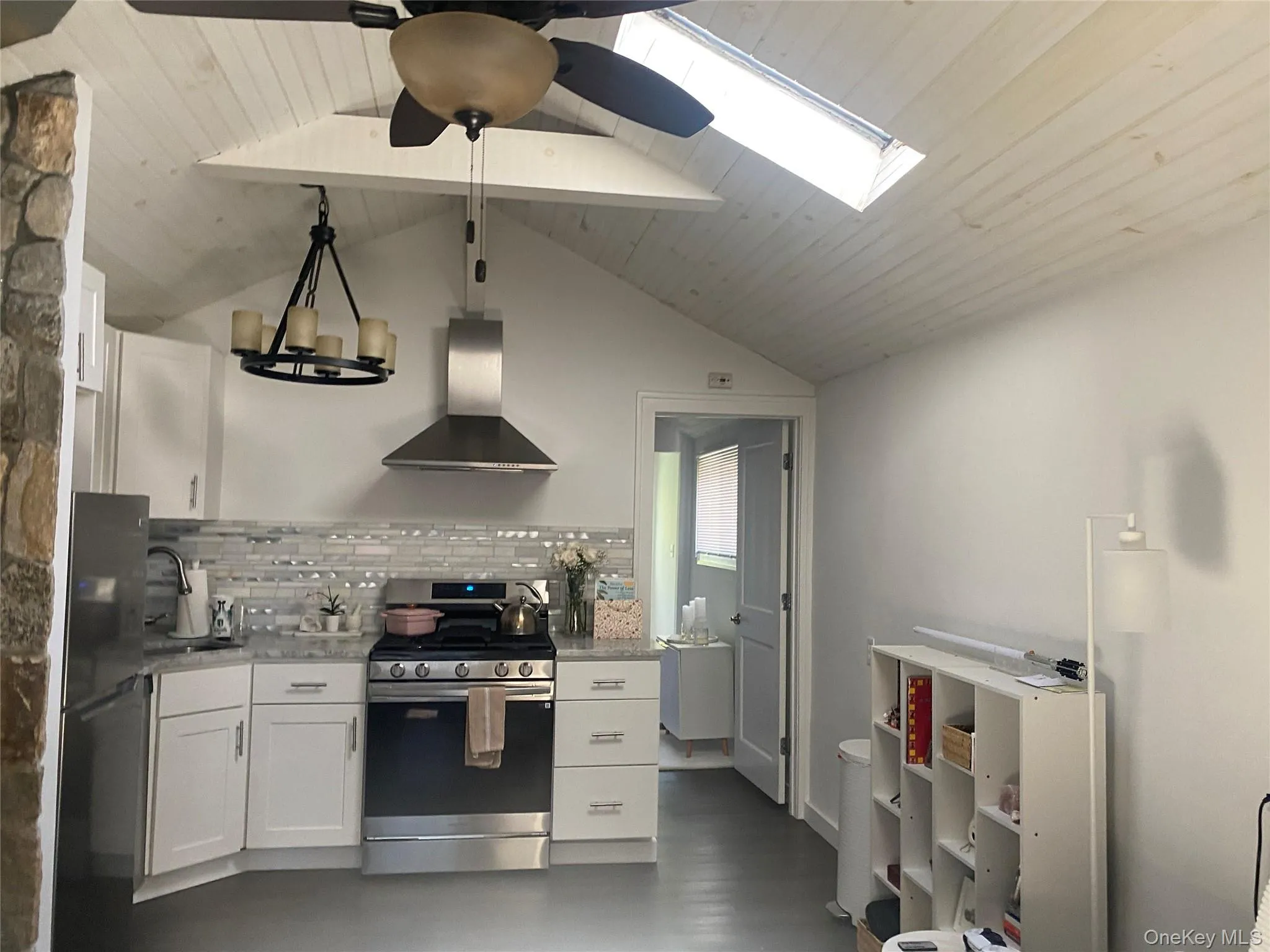 Kitchen featuring gas range oven, white cabinetry, backsplash, wall chimney range hood, and a skylight Kitchen featuring gas range oven, white cabinetry, backsplash, wall chimney range hood, and a skylight