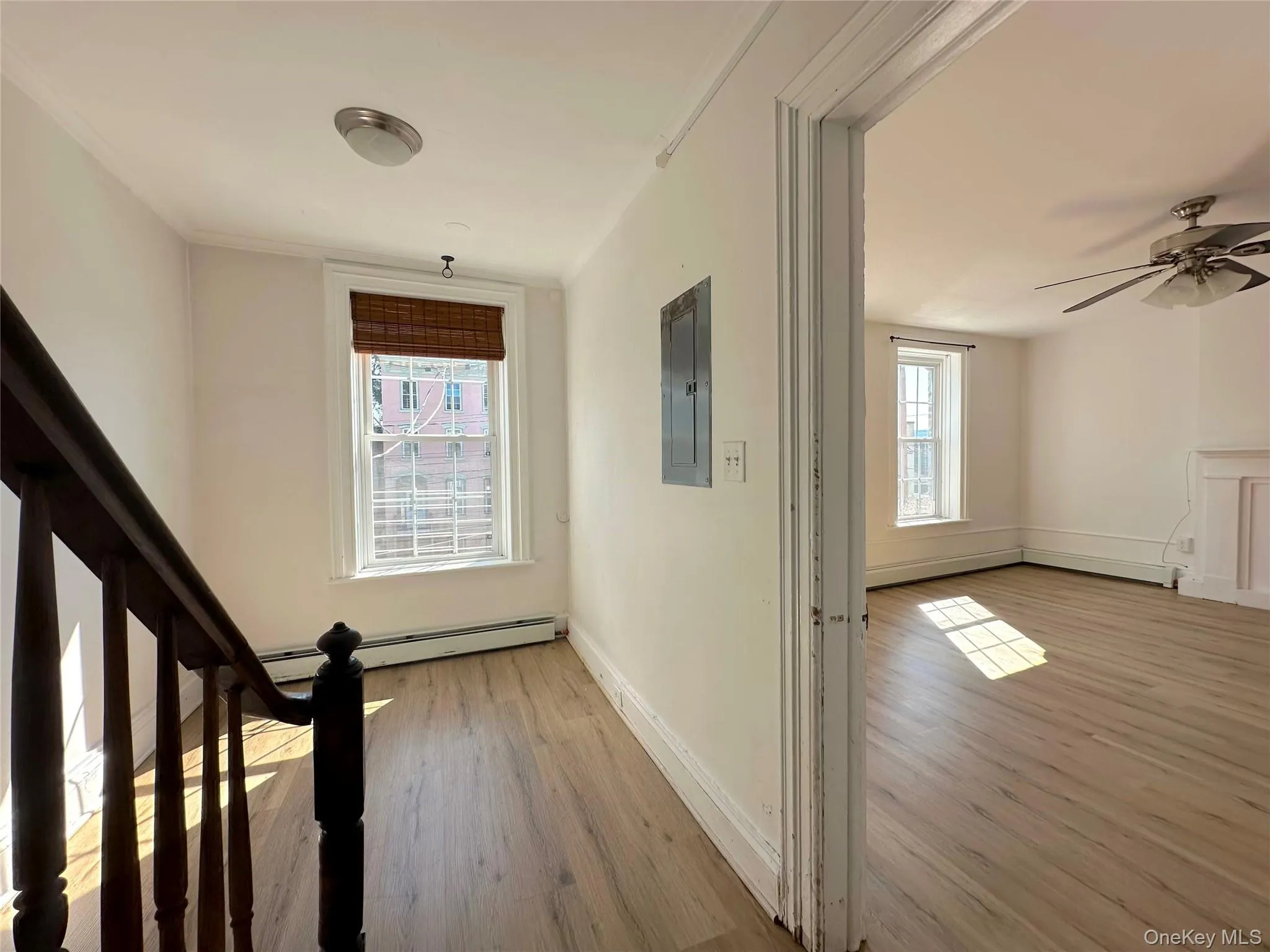 Corridor featuring light wood-style flooring, healthy amount of natural light, electric panel, and stairway Corridor featuring light wood-style flooring, healthy amount of natural light, electric panel, and stairway