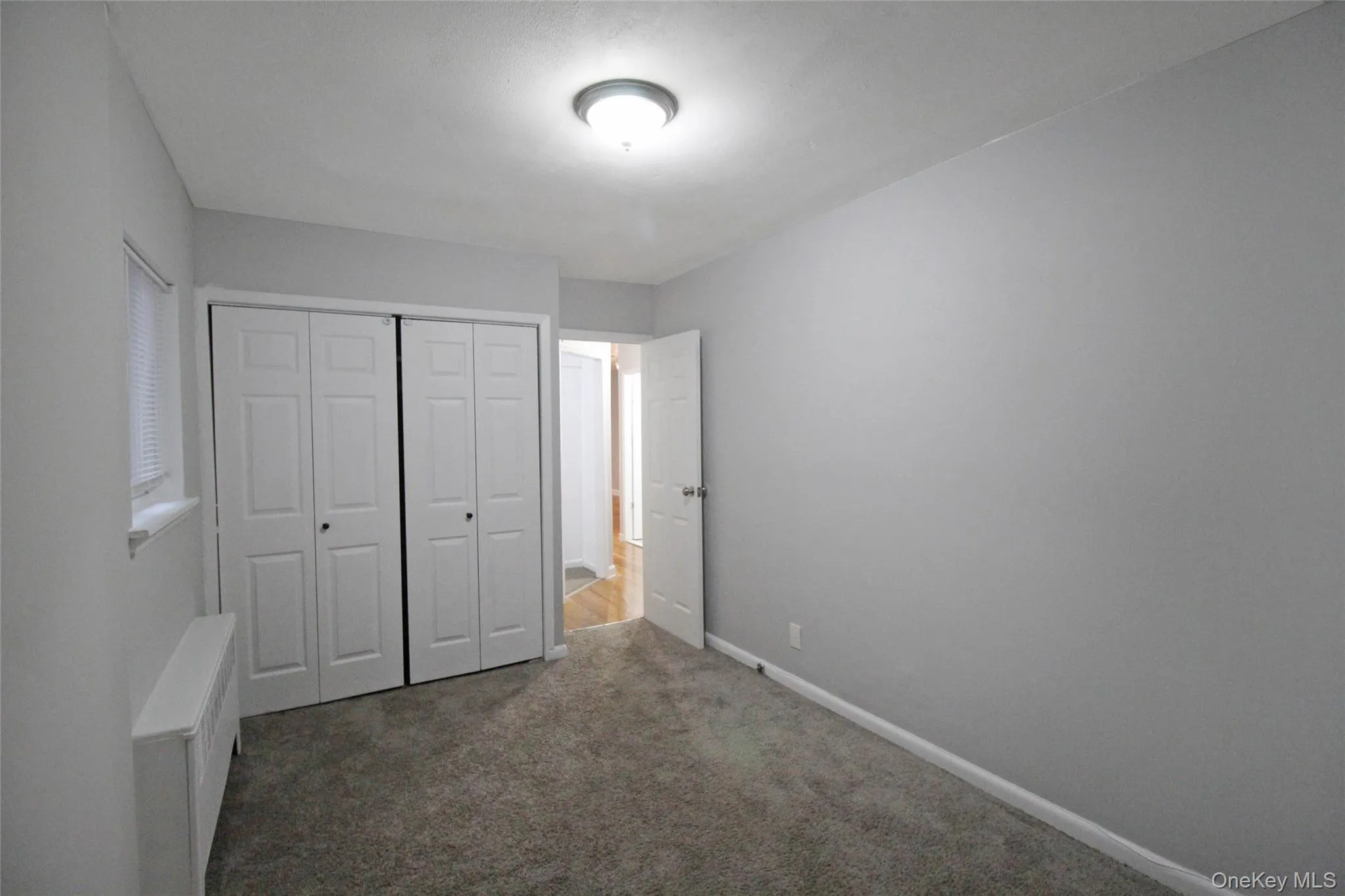 Unfurnished bedroom featuring dark colored carpet, a closet, and radiator Unfurnished bedroom featuring dark colored carpet, a closet, and radiator