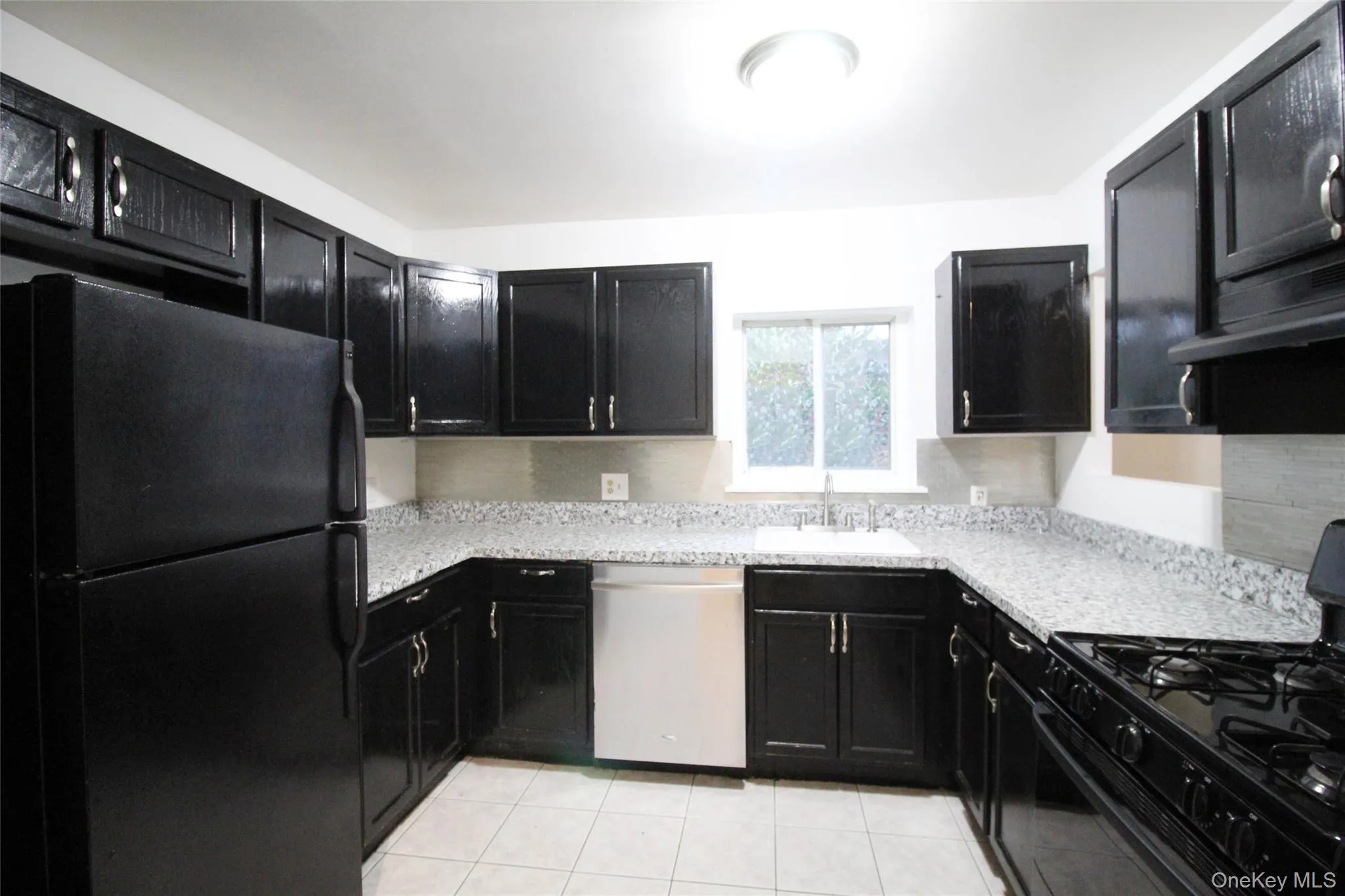 Kitchen with dark cabinets, black appliances, light tile patterned floors, light stone counters, and range hood Kitchen with dark cabinets, black appliances, light tile patterned floors, light stone counters, and range hood