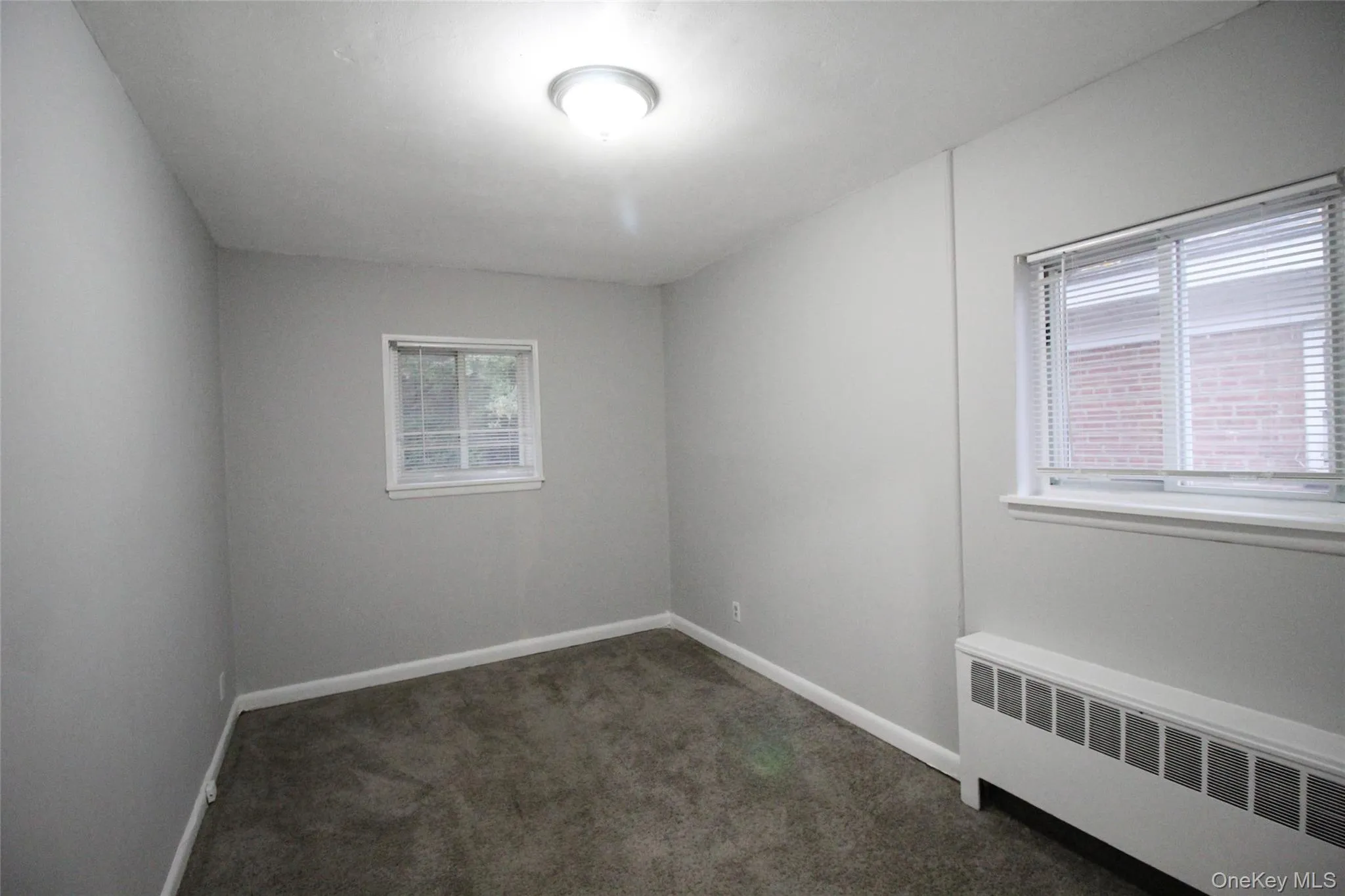 Unfurnished room featuring radiator heating unit and dark carpet Unfurnished room featuring radiator heating unit and dark carpet