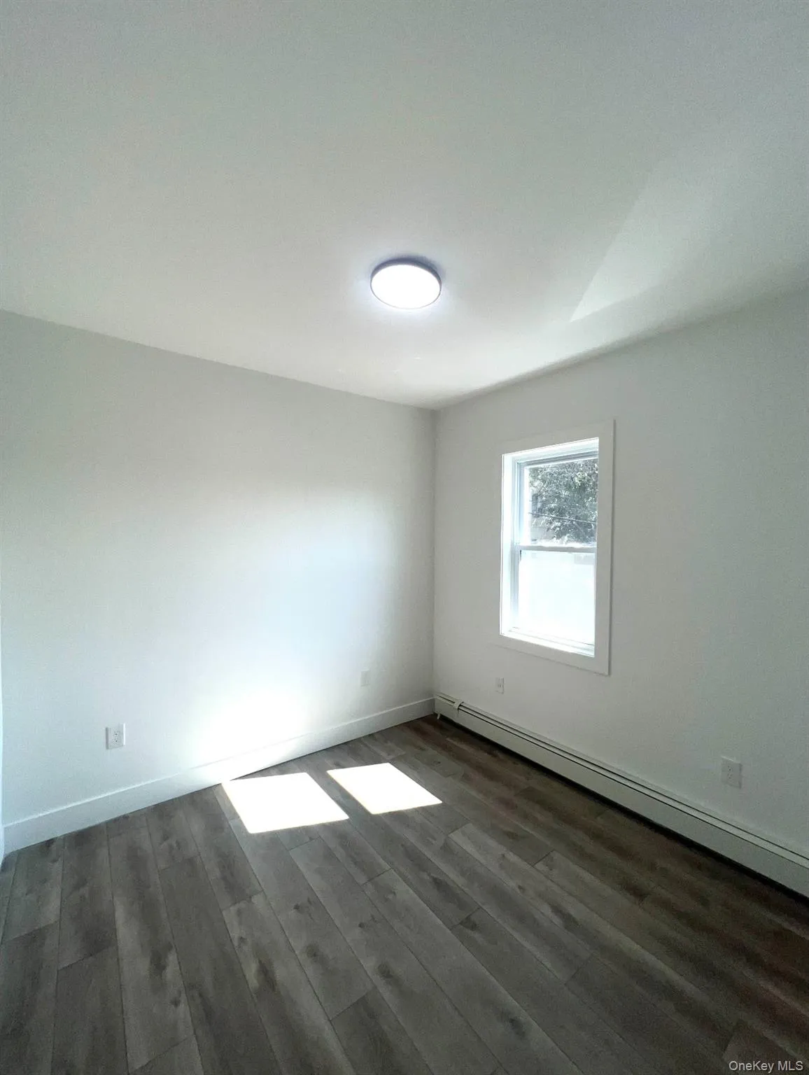 Empty room with a baseboard radiator and dark wood finished floors Empty room with a baseboard radiator and dark wood finished floors